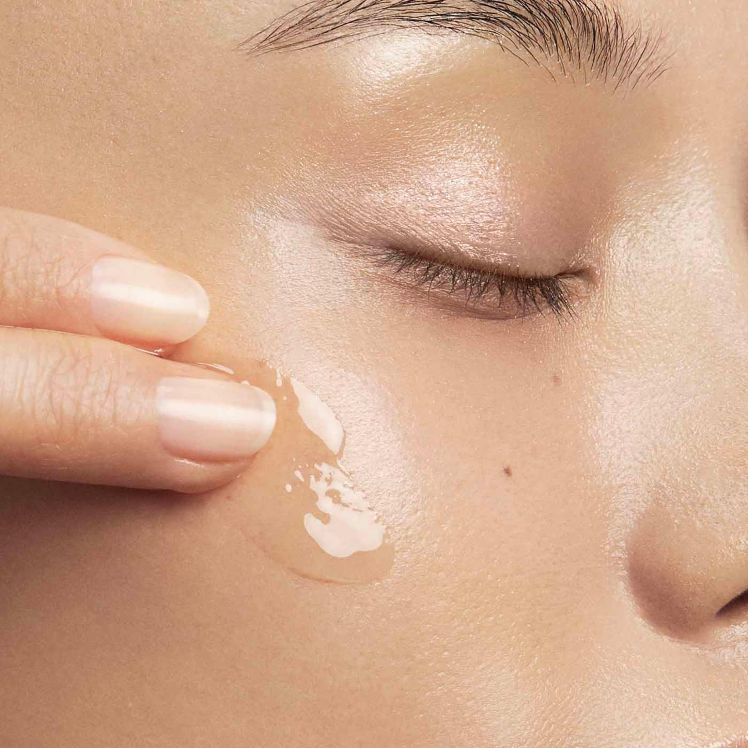 Primo piano di una zona della pelle. Una mano applica un liquido trasparente sulla pelle.