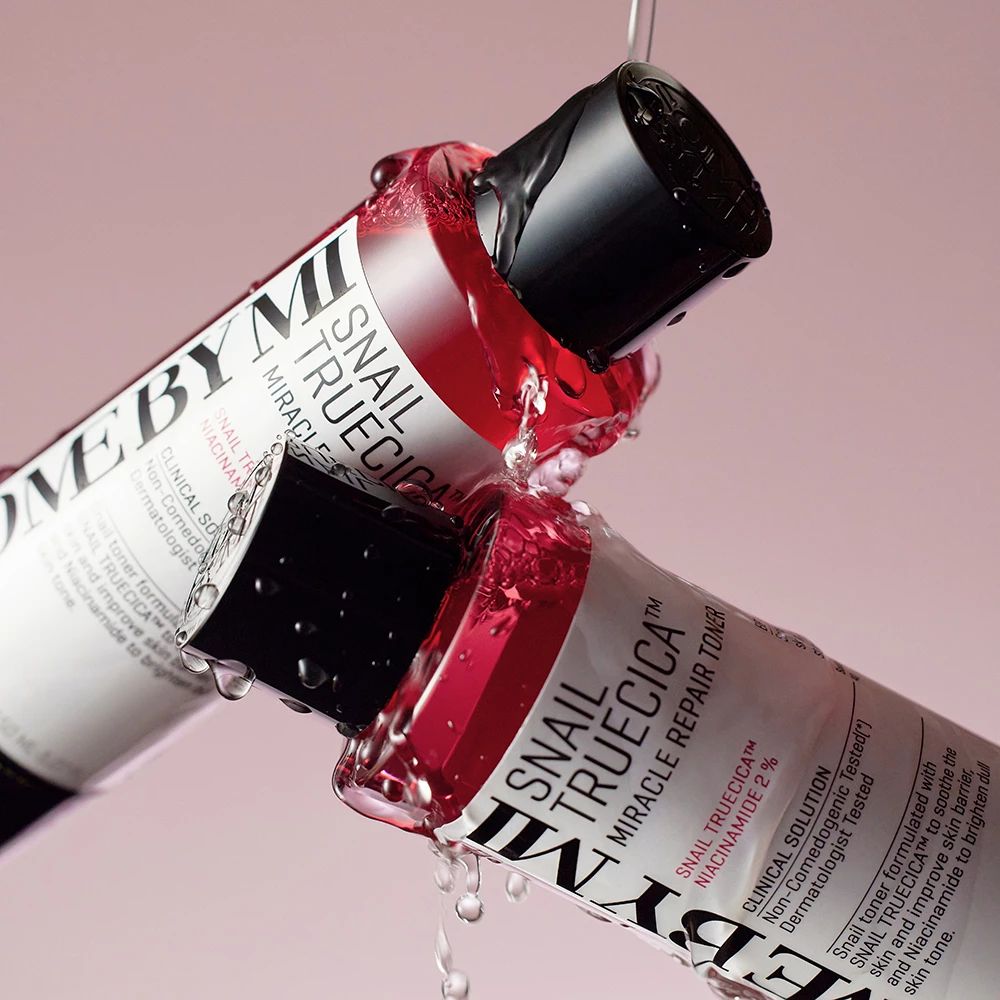 Due flaconi di tonico riparatore Some By Mi Snail Truecica Miracle con tappo nero, circondati da acqua. Liquido rosso visibile.