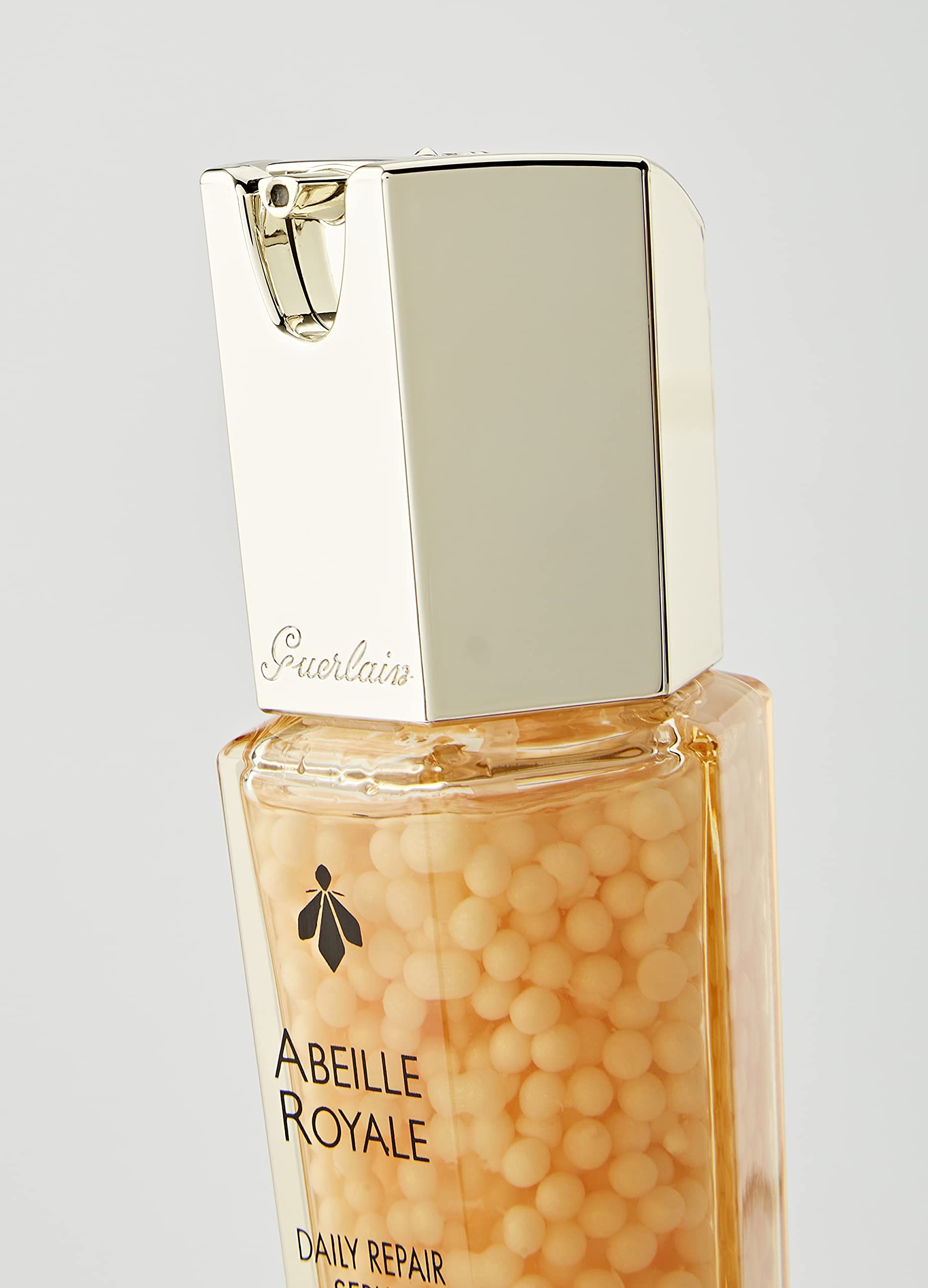 Primo piano del flacone di siero. Scritta: Abeille Royale, Guerlain. Tappo dorato.