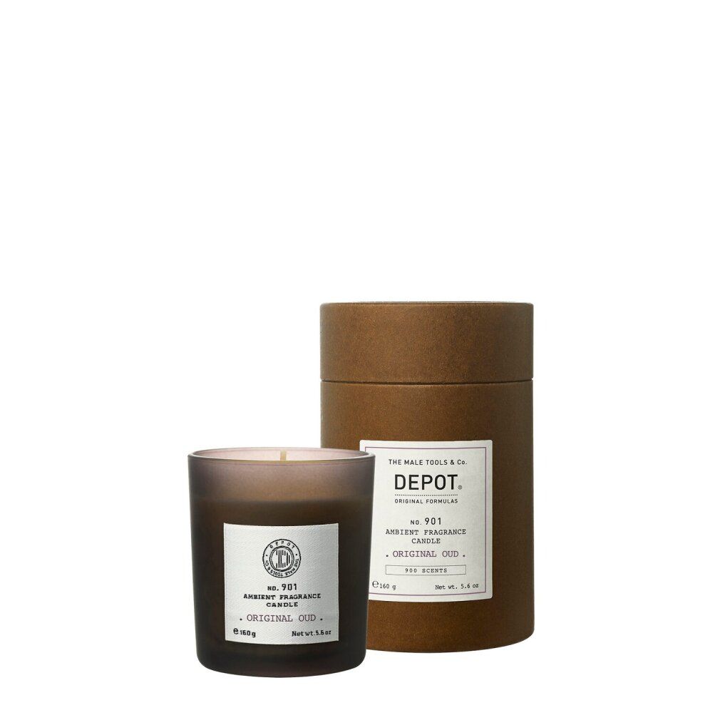Candela marrone in vetro, accanto a confezione cilindrica. Entrambi con etichette. Testo: Depot 901 Ambient Fragrance Candle.