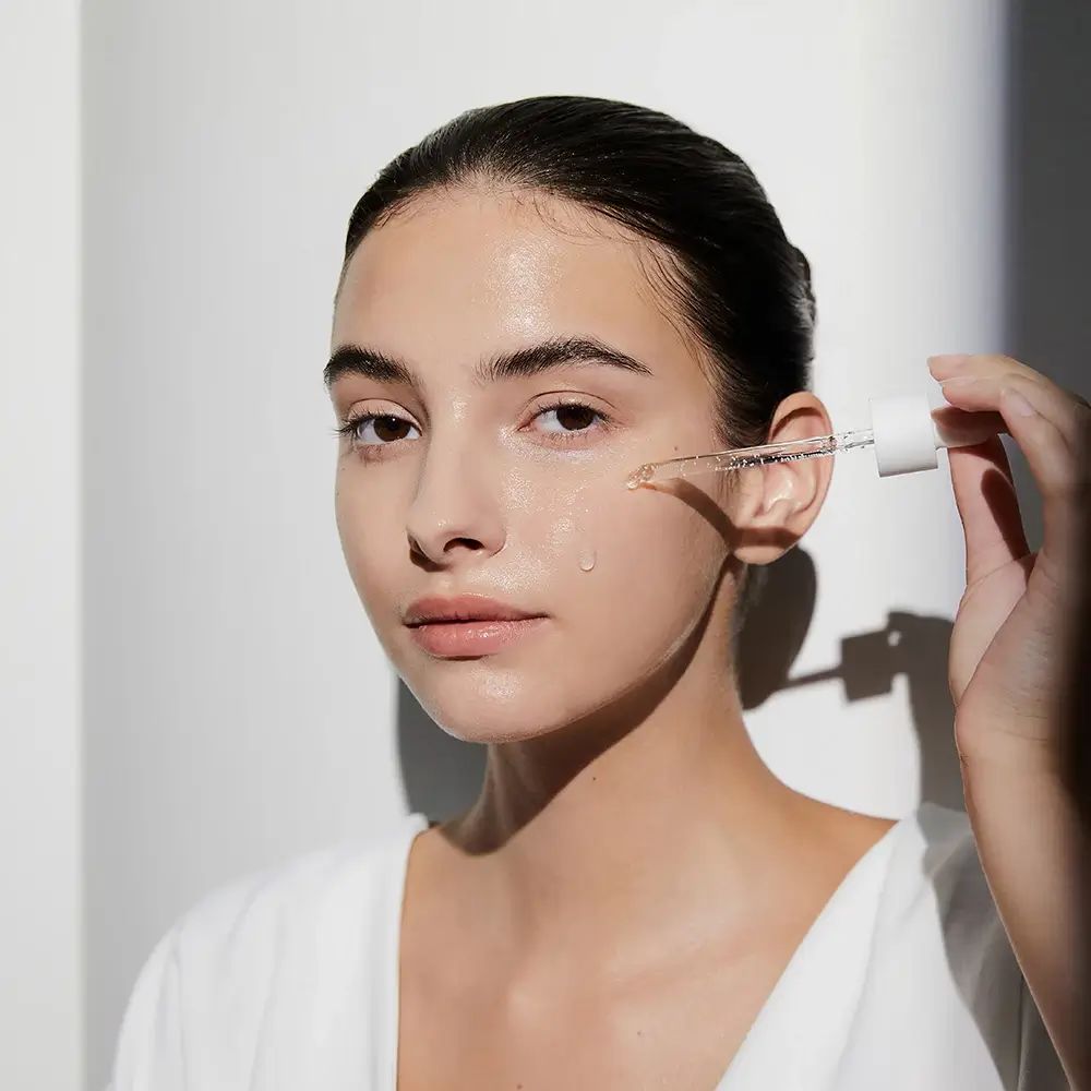 Donna con prodotto per la cura della pelle. Pipetta con liquido. Nome del prodotto non visibile.