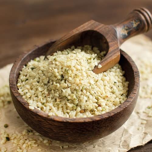 Ciotola di legno con semi di canapa sgusciati e paletta di legno. Su carta marrone.