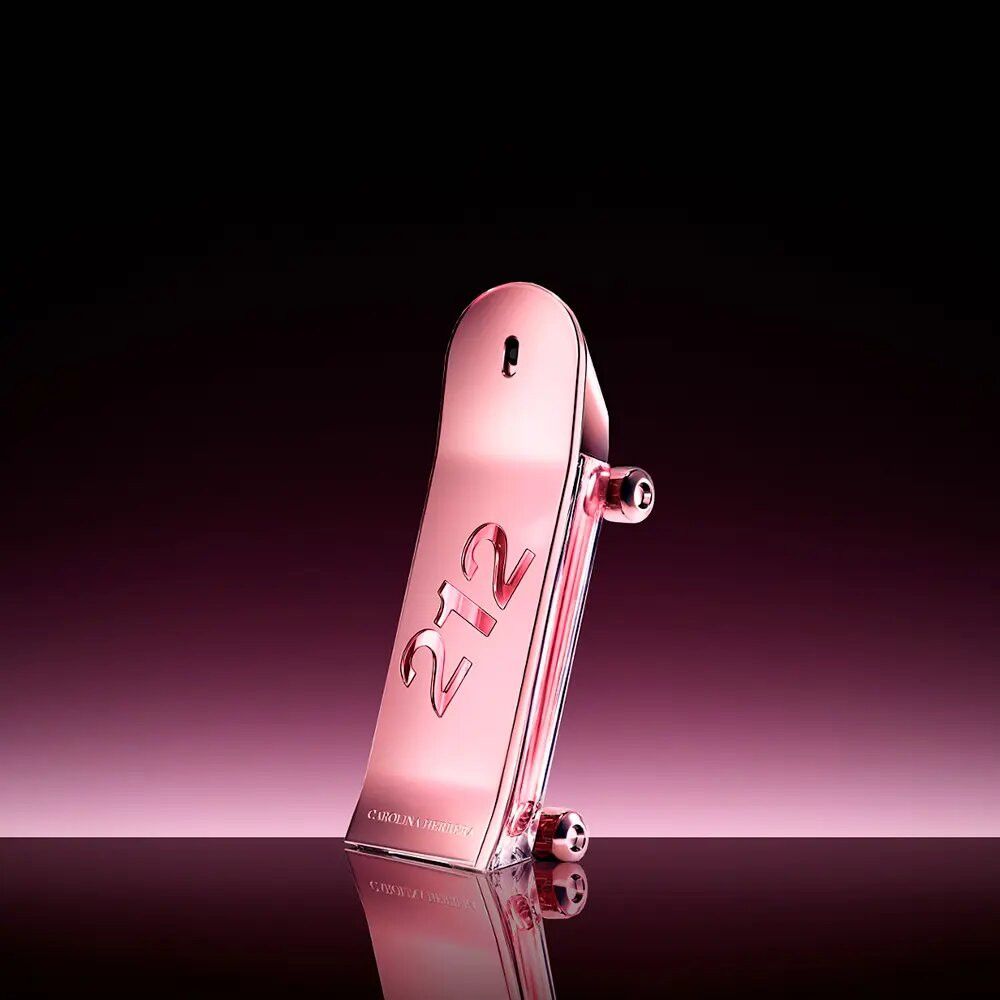 Flacone rosa a forma di skateboard. Scritta "212". Due ruote laterali. Riflessi su sfondo scuro.