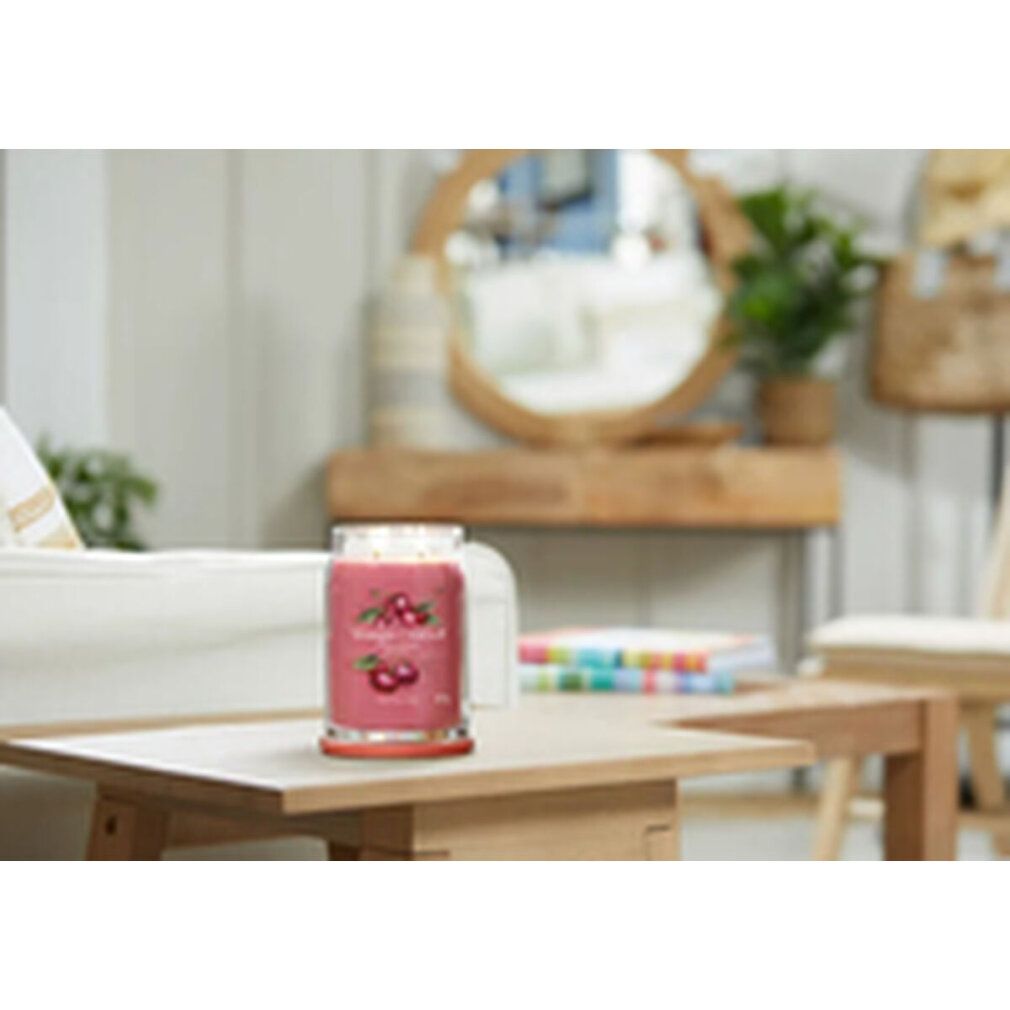 Candela profumata su tavolo. Decorazione ciliegia e scritta. Base rossa. Contesto soggiorno.