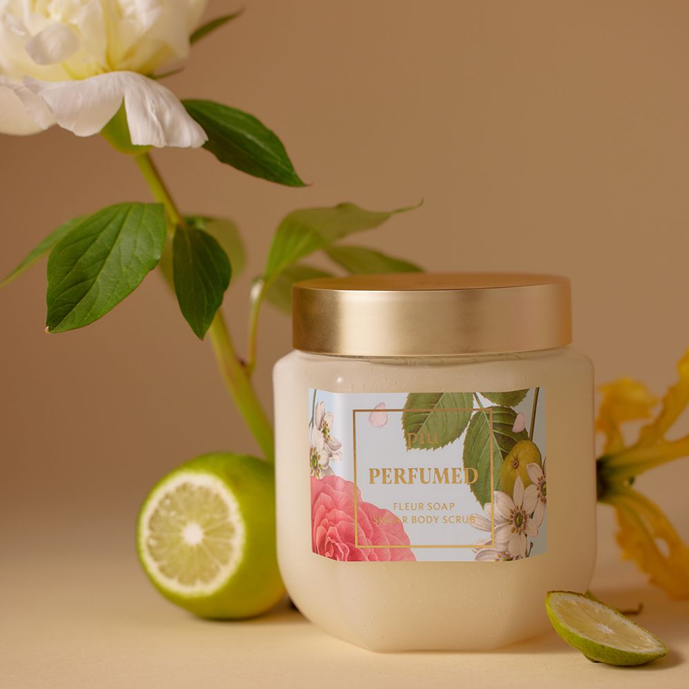 Vaso con coperchio dorato, etichetta floreale. Fetta di lime e fiori accanto al prodotto.