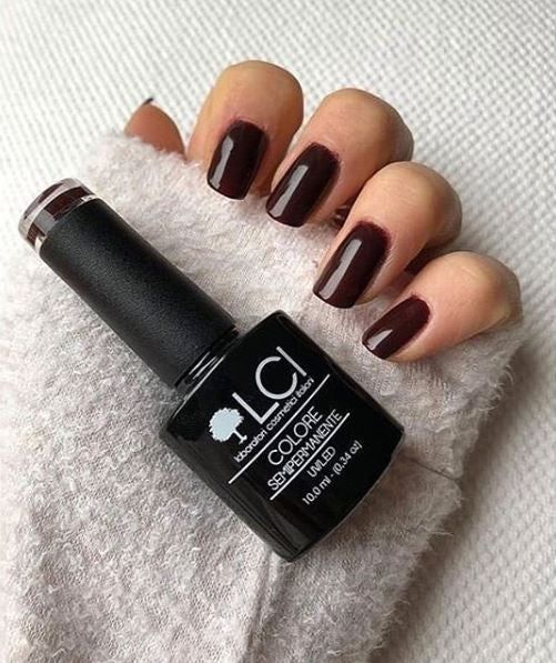 Mano con unghie smaltate e flacone di smalto. Colore: rosso-marrone. Scritta: LCI, Colore Semipermanente, UVLED 10,0 ml.