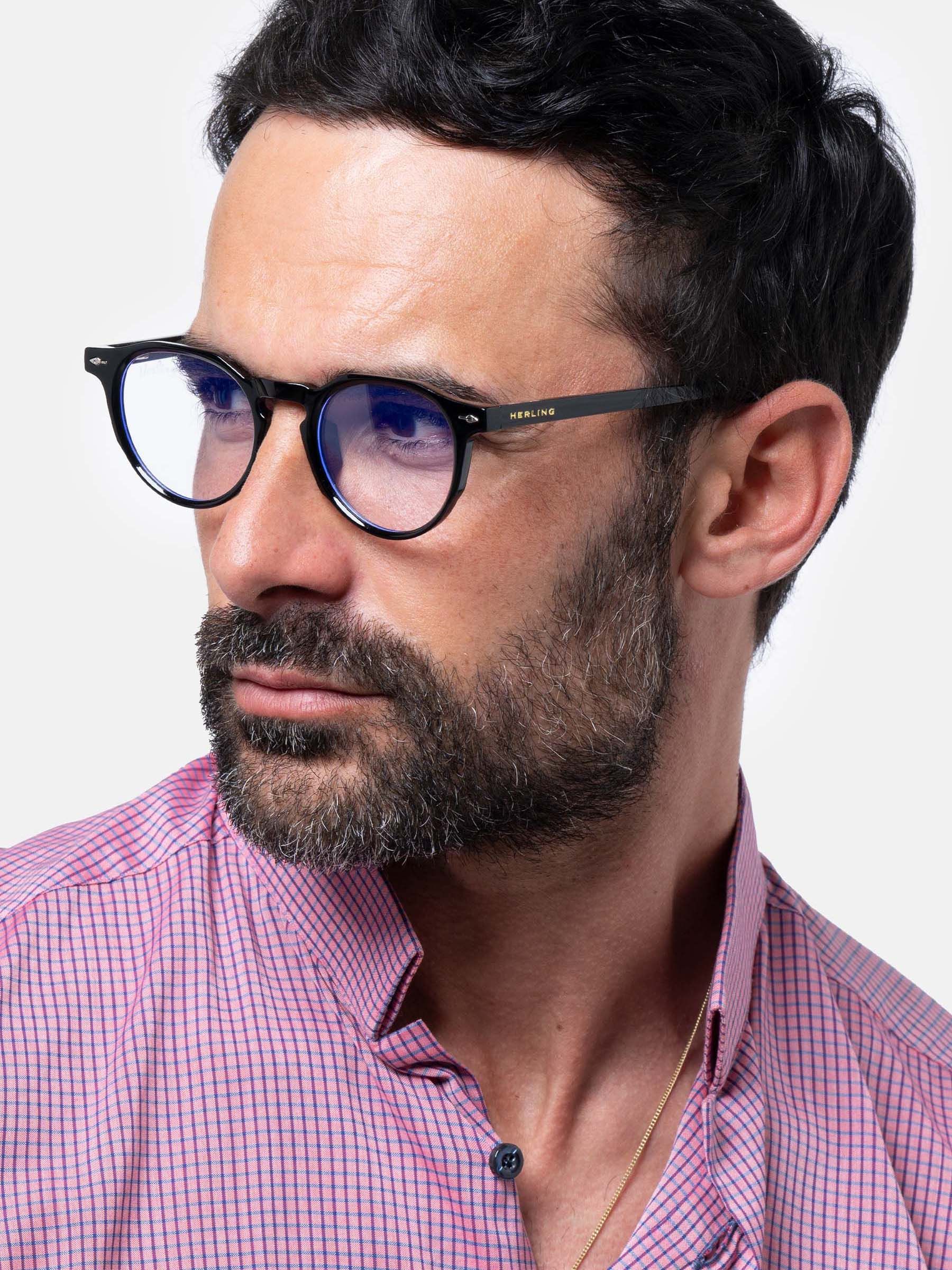 Uomo con occhiali neri con lenti rotonde. Marchio Herling sulla stanghetta. Modello unisex.