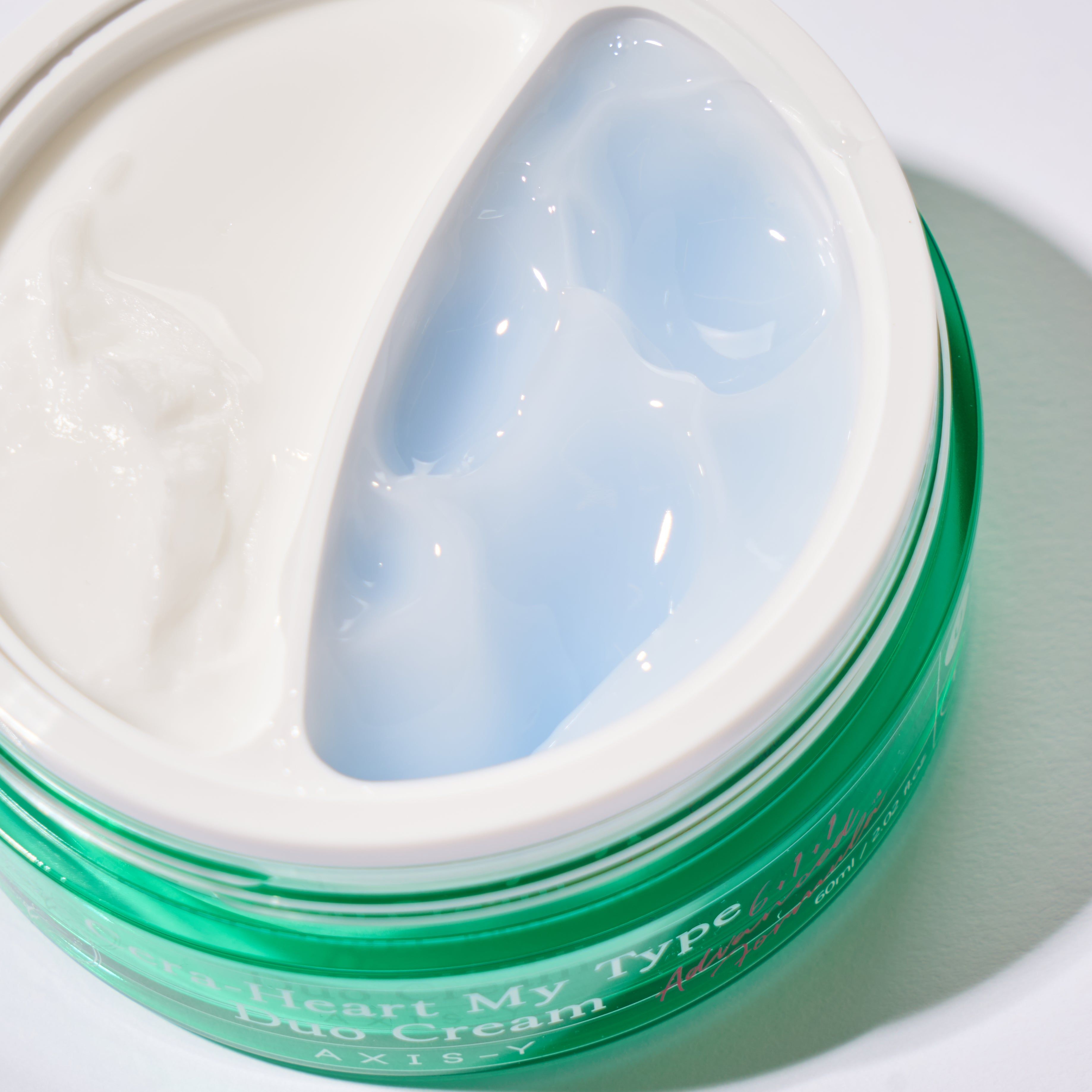 Vaso di crema aperto, diviso in creme bianca e blu. Vaso verde, coperchio bianco. Nessuna scritta.