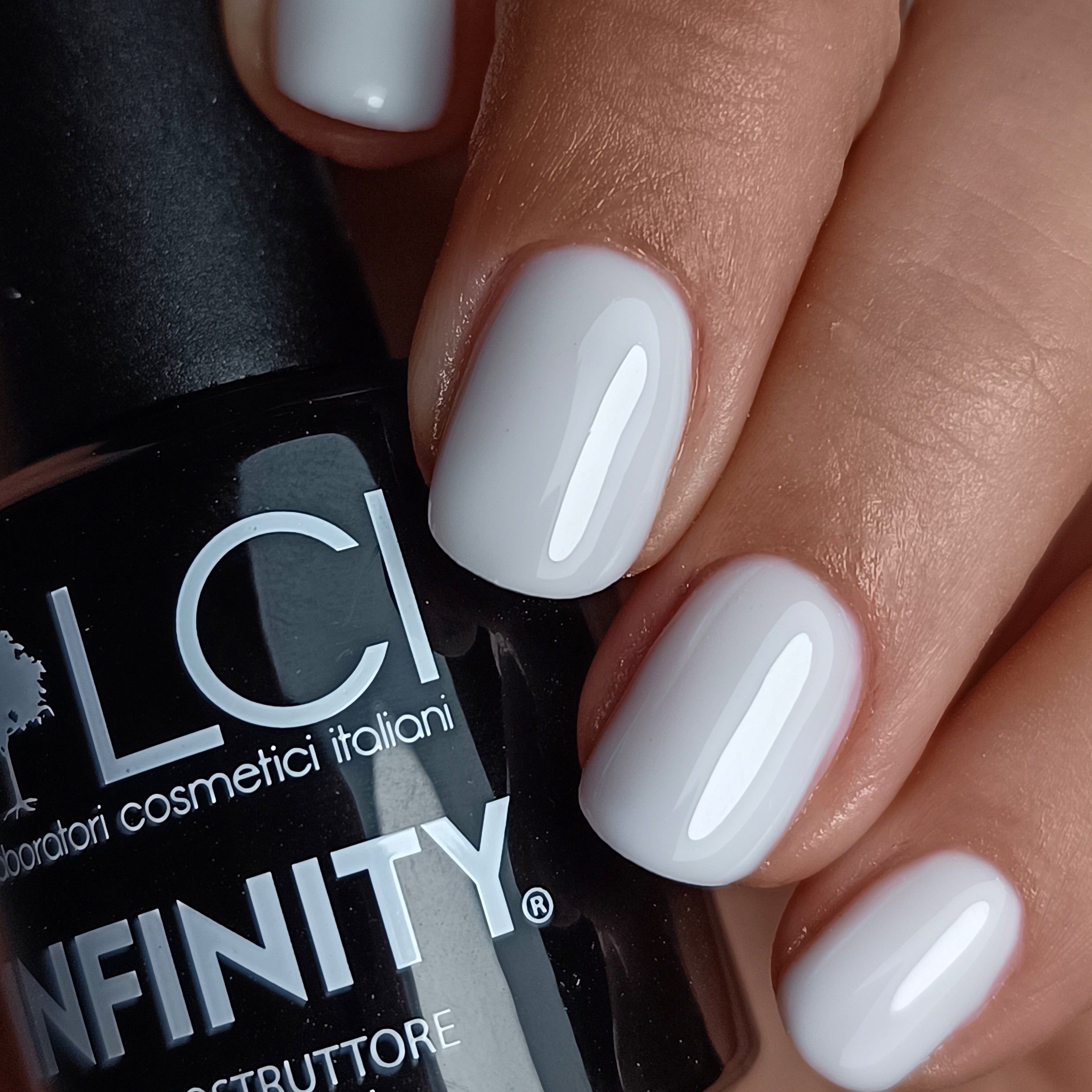 Mano con unghie smaltate e flacone. Unghie smaltate con gel bianco. Flacone: LCI INFINITY Builder Gel.