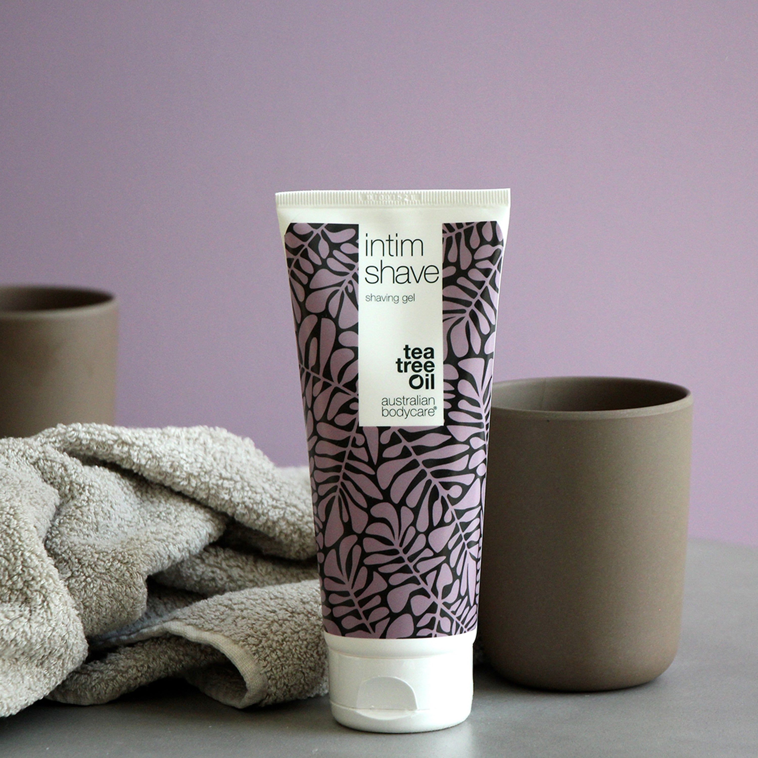 Tubo di gel da barba Intim Shave, accanto a tazze e asciugamano. Testo: Tea Tree Oil, Australian Bodycare.