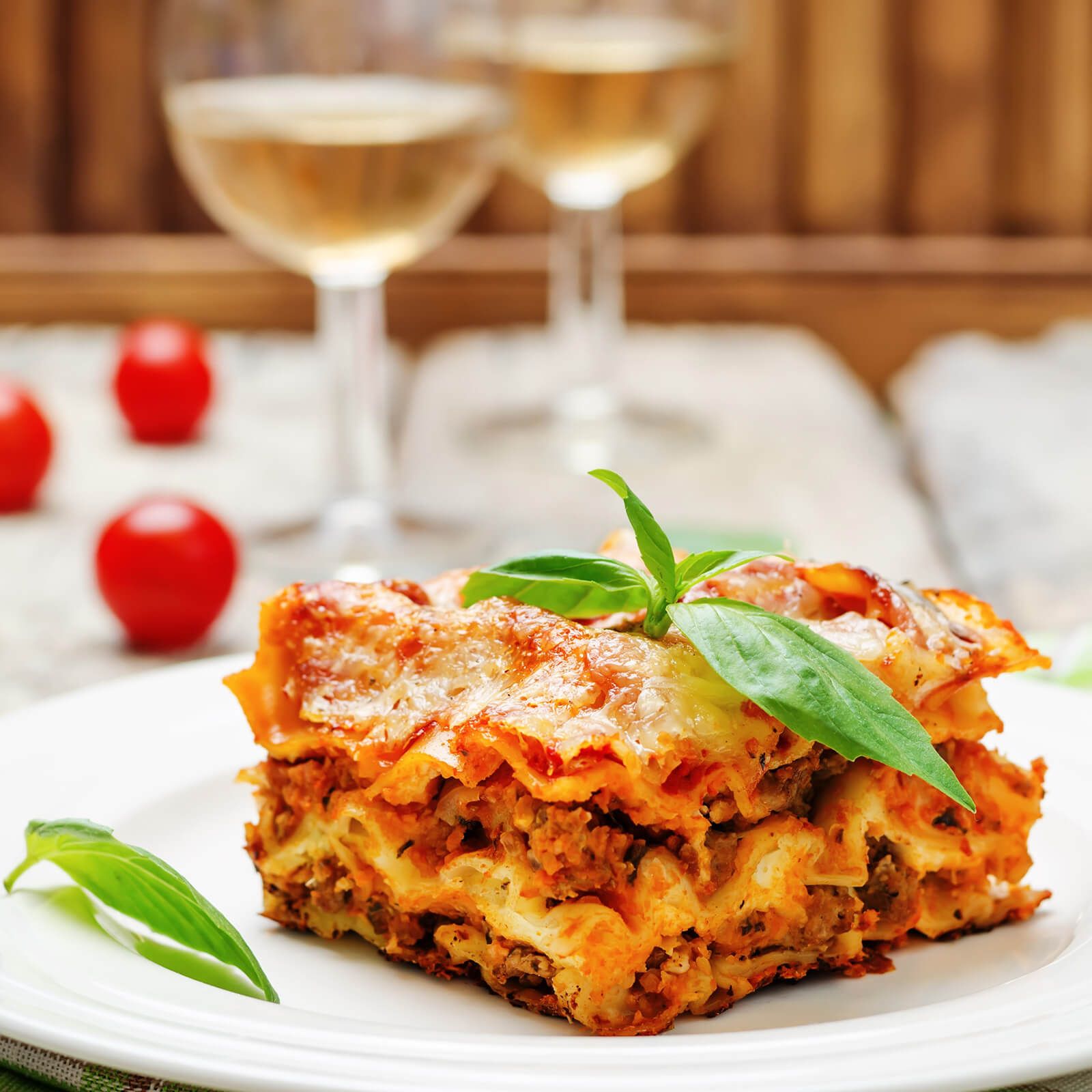 Porzione di lasagne su piatto bianco. Strati di pasta, carne e formaggio. Guarnita con basilico.