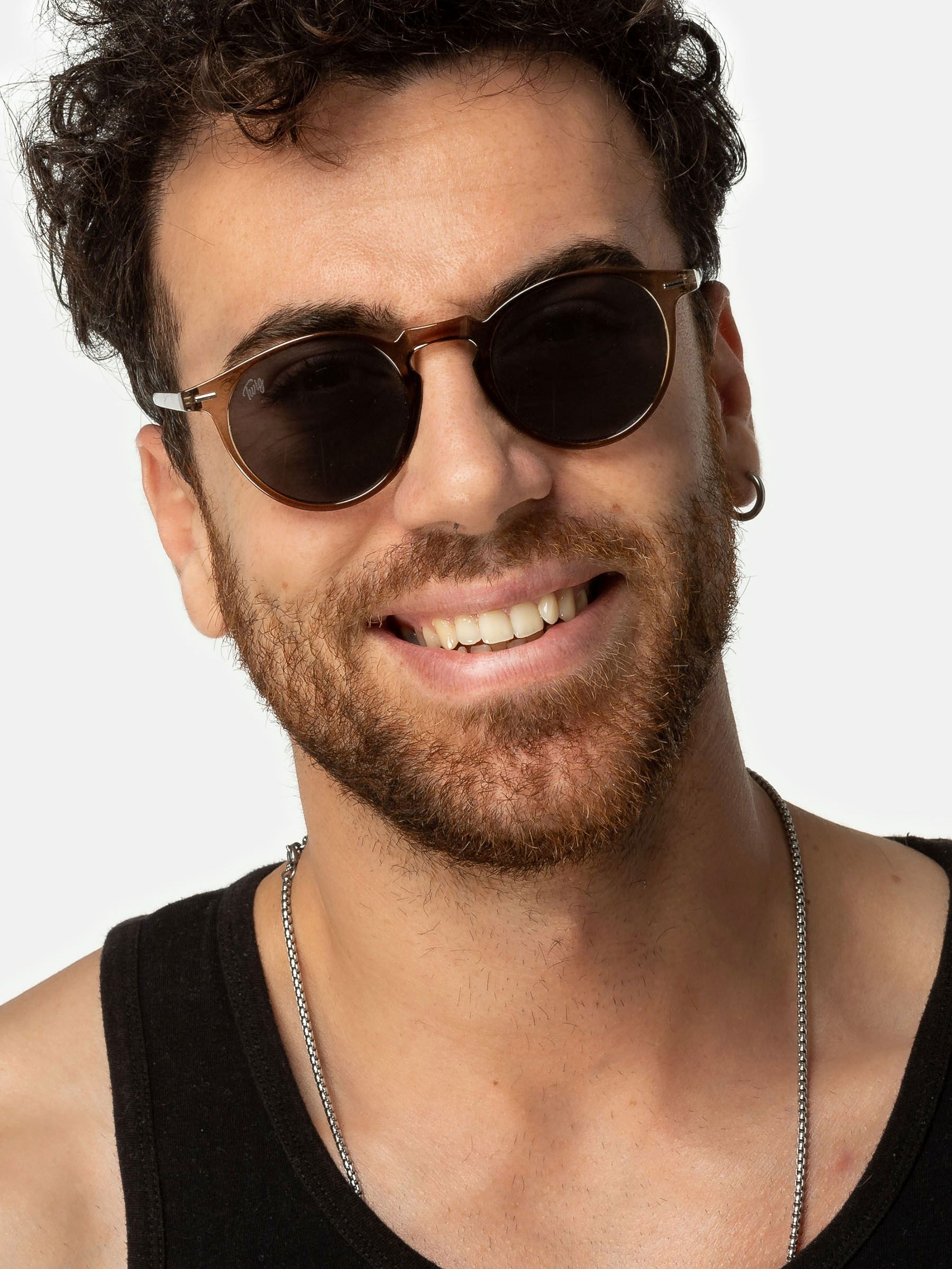 Uomo con occhiali da sole Twig. Montatura marrone, lenti scure, sorridente.