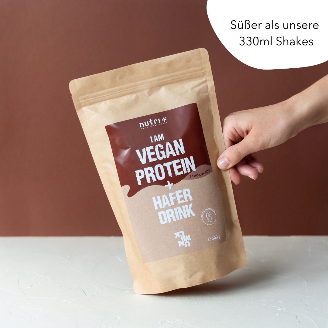Busta beige con 'I AM VEGAN PROTEIN + HAFER DRINK'. Stampa marrone. Mano che tiene la busta. Testo: 'Süßer als unsere 330ml Shakes'.