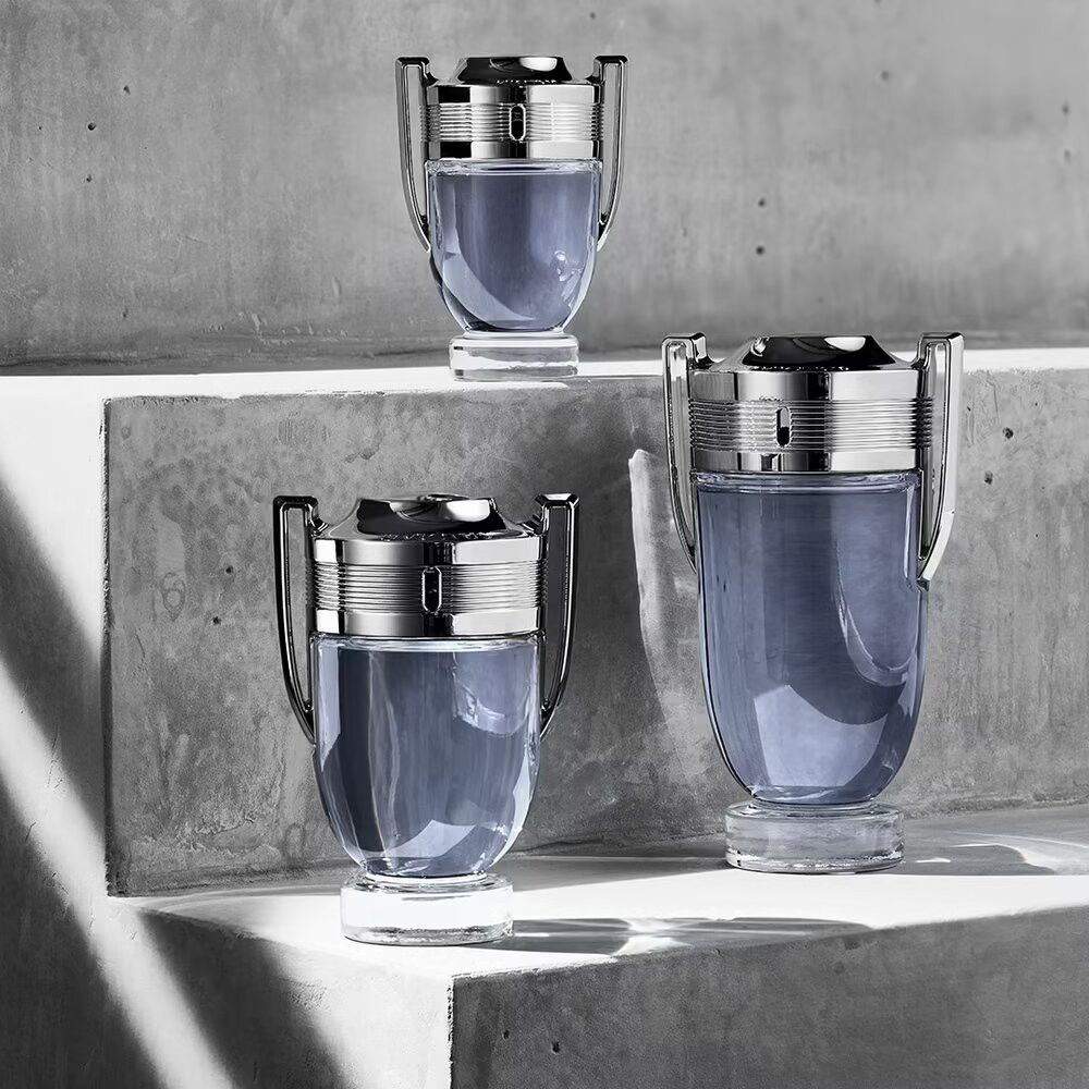 Tre flaconi INVICTUS con tappi argentati su una superficie grigia. Diverse dimensioni.