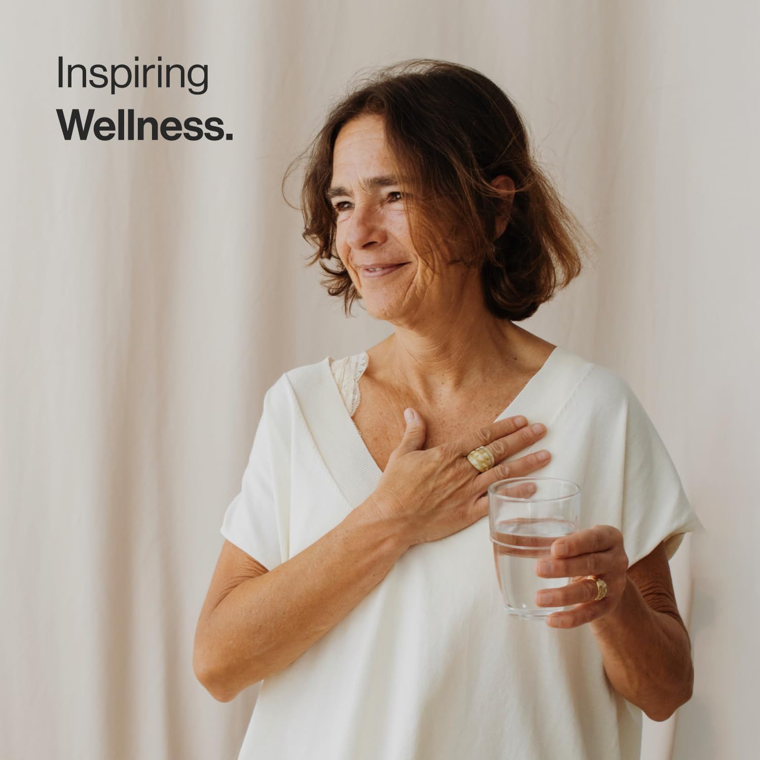Donna che tiene un bicchiere d'acqua. Testo: Inspiring Wellness.