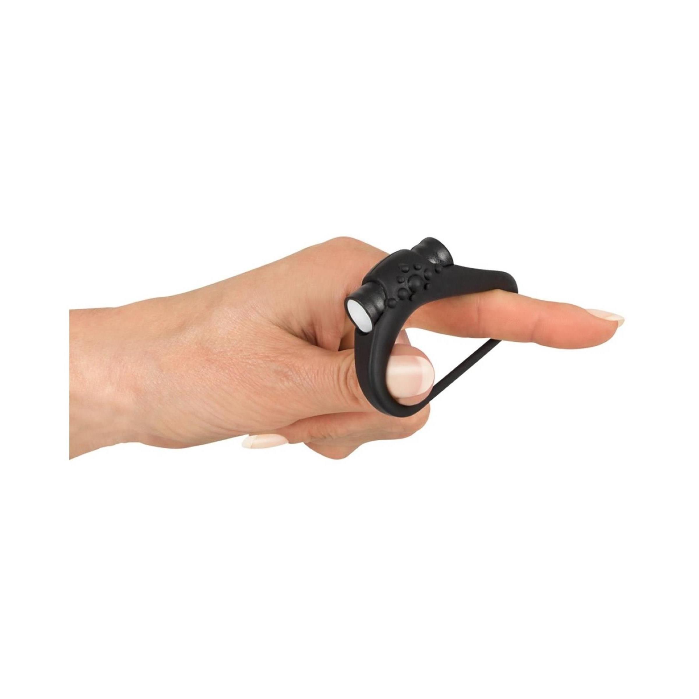 Anello fallico nero su un dito. Anello con nodi e due elementi bianchi.