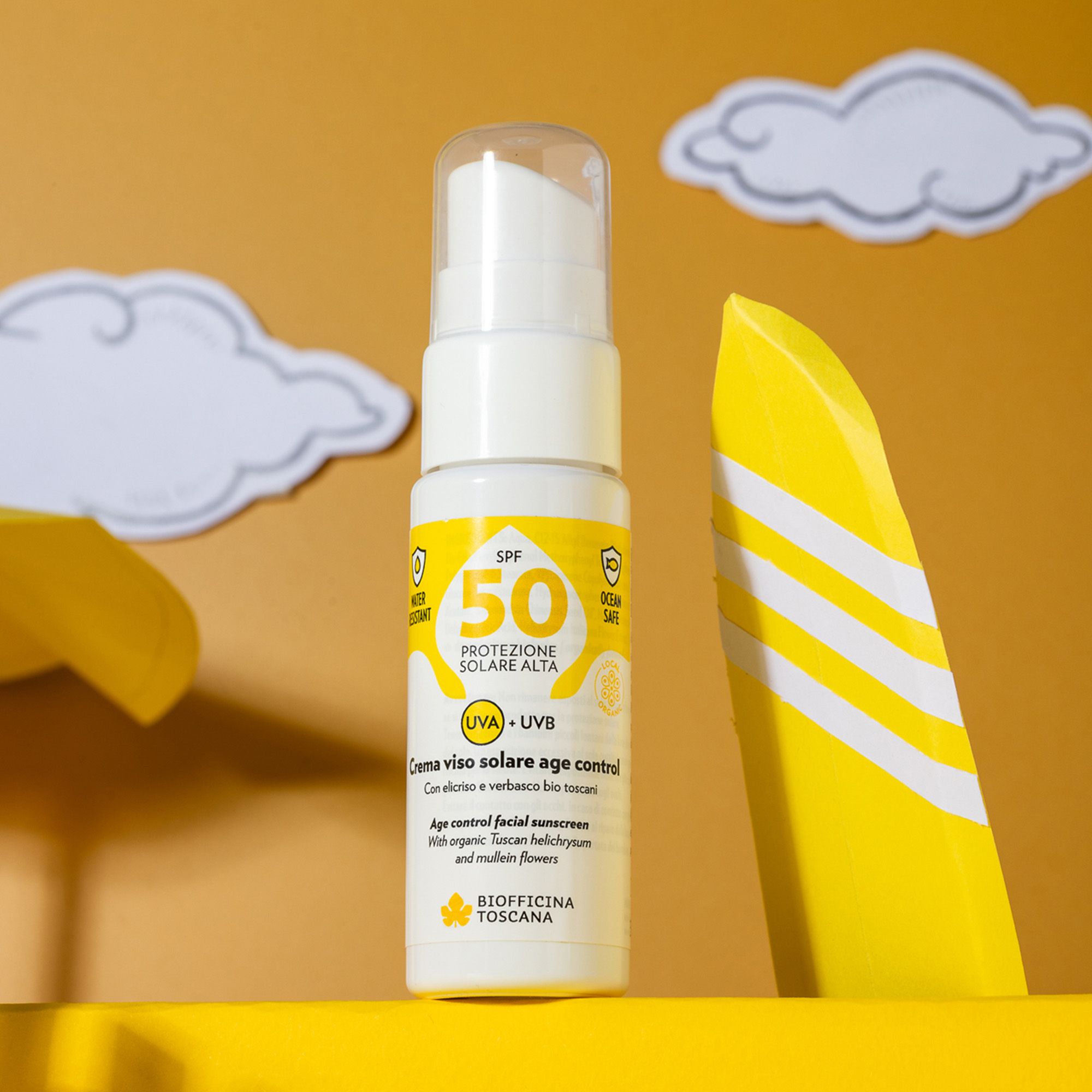 Flacone spray bianco con etichetta gialla. Testo: SPF 50, protezione solare, UVA+UVB. Marchio: Biofficina Toscana. Sfondo giallo.