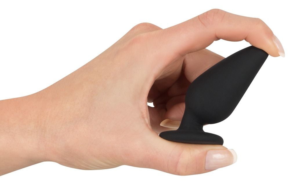 Mano che tiene un plug anale nero. Forma conica, base piatta. Colore della pelle.