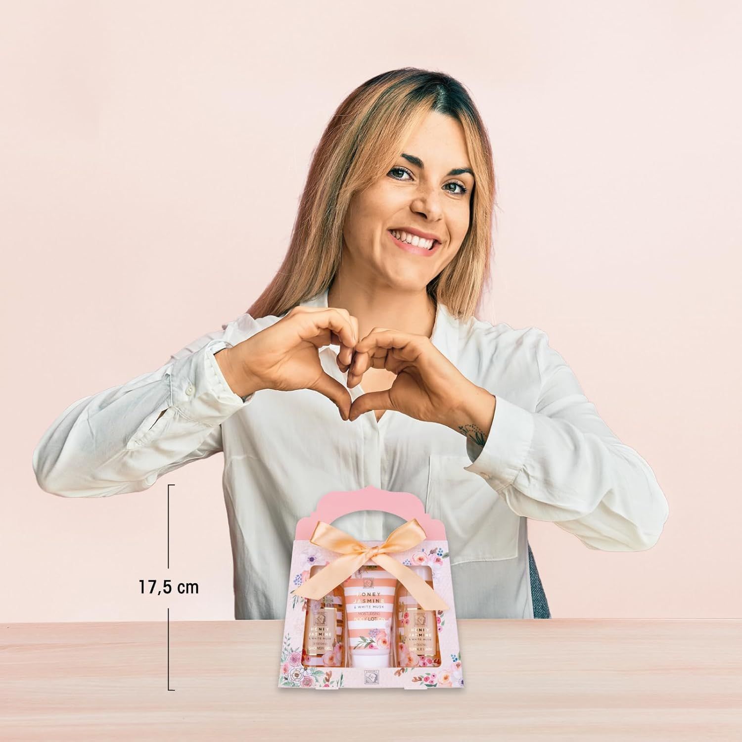 Donna forma un cuore con le mani. Confezione regalo con tre prodotti: gel doccia, bagno schiuma, lozione per il corpo. Scatola con fiocco e motivi floreali.