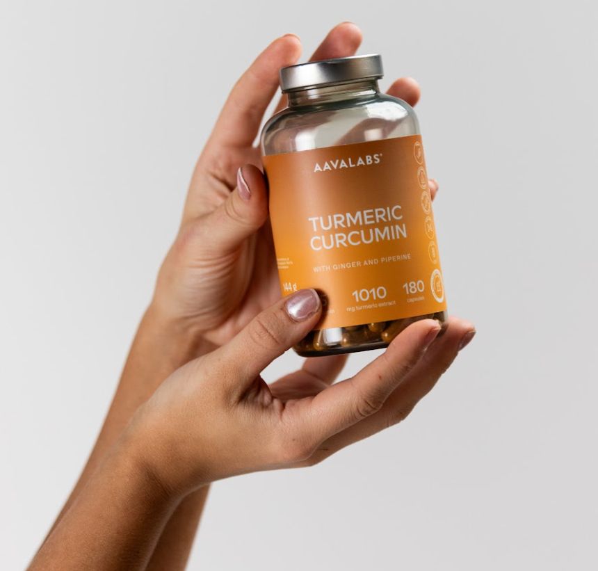 Mani che tengono un flacone di capsule di curcuma. L'etichetta mostra 'Turmeric Curcumin'.