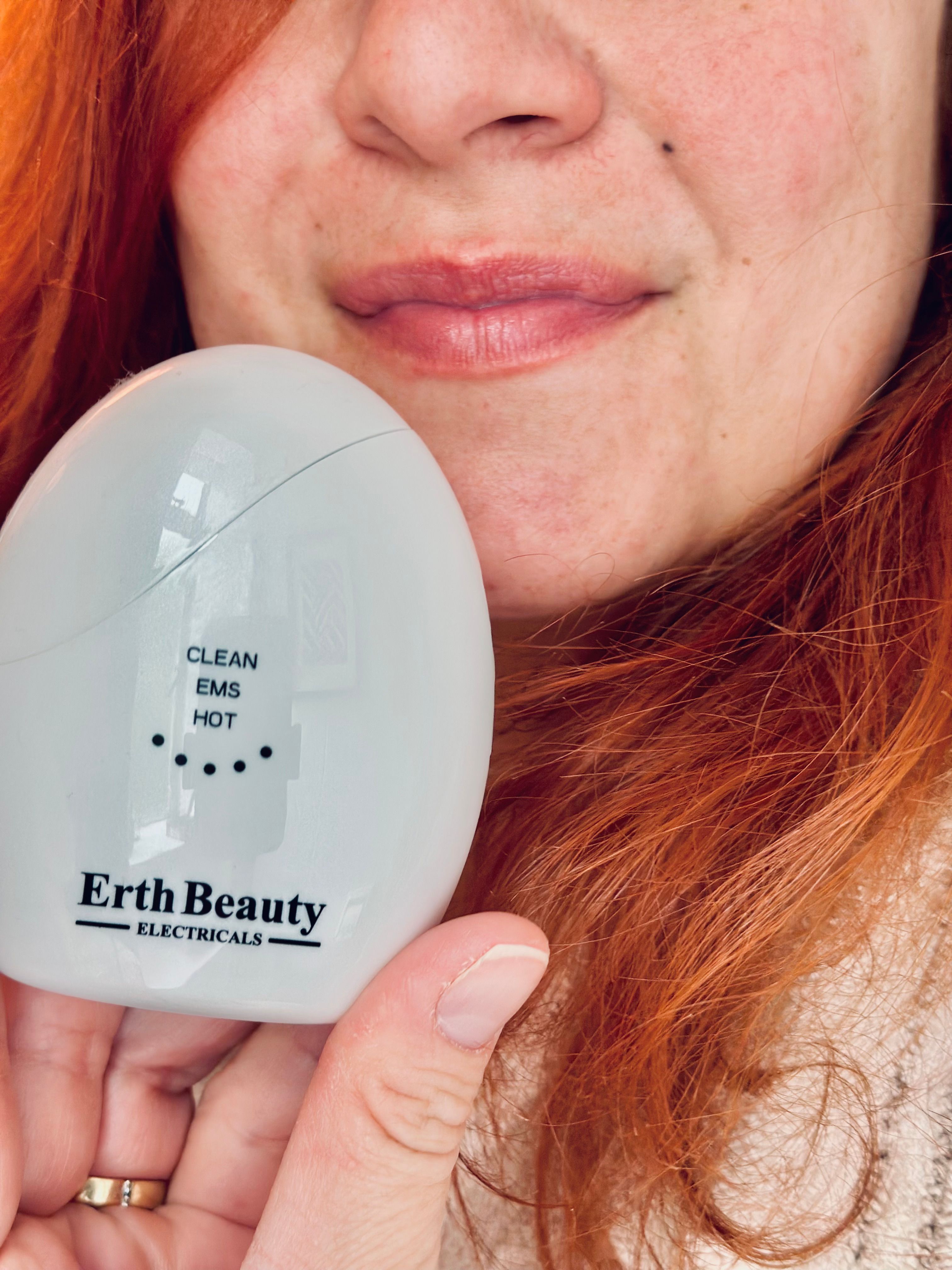 Dispositivo ovale bianco con scritta: CLEAN, EMS, HOT. Marchio: Erth Beauty Electricals. Dispositivo tenuto.