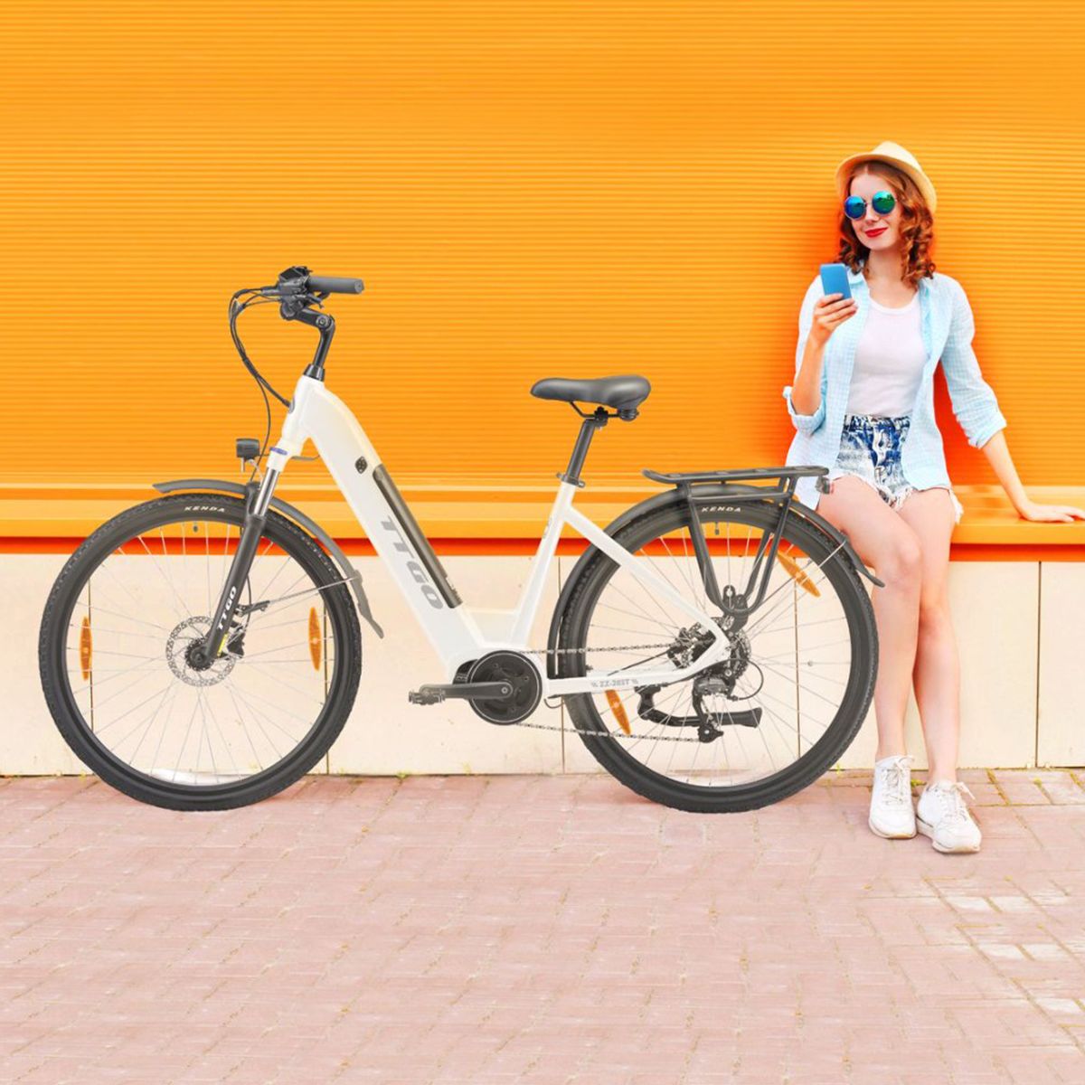 Una donna seduta accanto a una e-bike bianca. La bici ha pneumatici neri e un portapacchi.