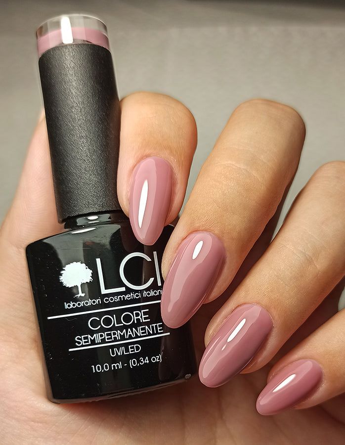 Mano con unghie smaltate e flacone di smalto. LCI Cosmetics, Hema Free, Rosso Tiziano. Unghie rosa-marrone, flacone accanto.