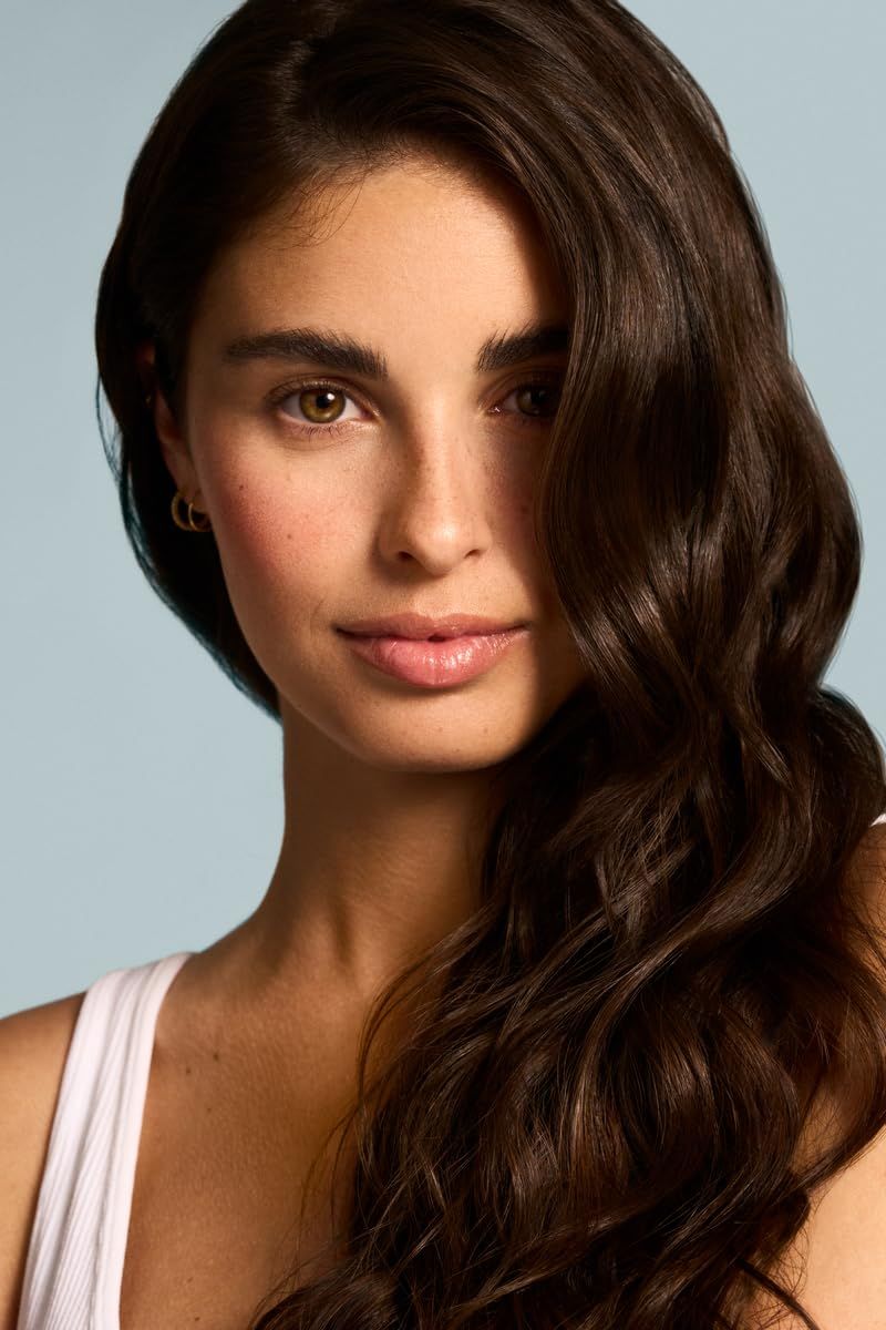 Ritratto di donna con lunghi capelli castani. Indossa una canotta bianca e guarda la fotocamera.