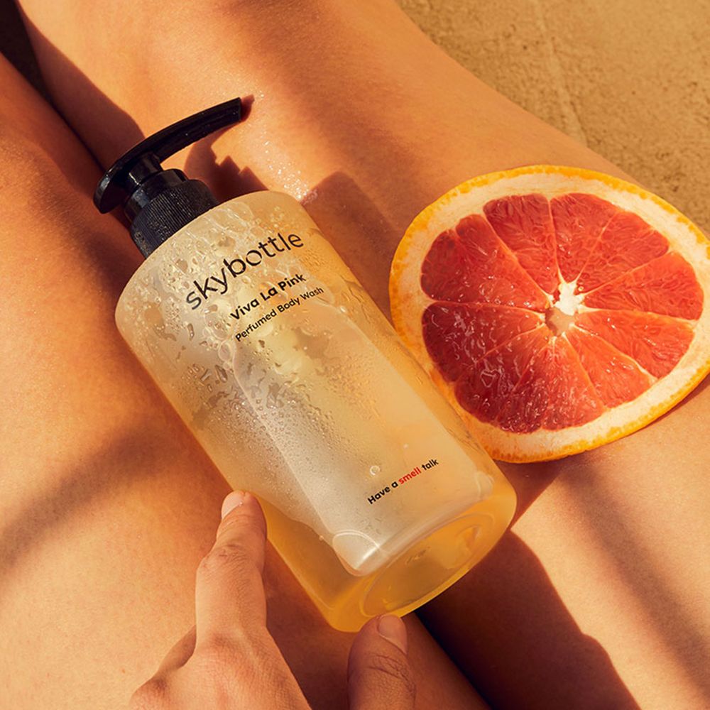 Gel doccia SKYBOTTLE Viva la Pink accanto a una fetta di pompelmo. Su una gamba.