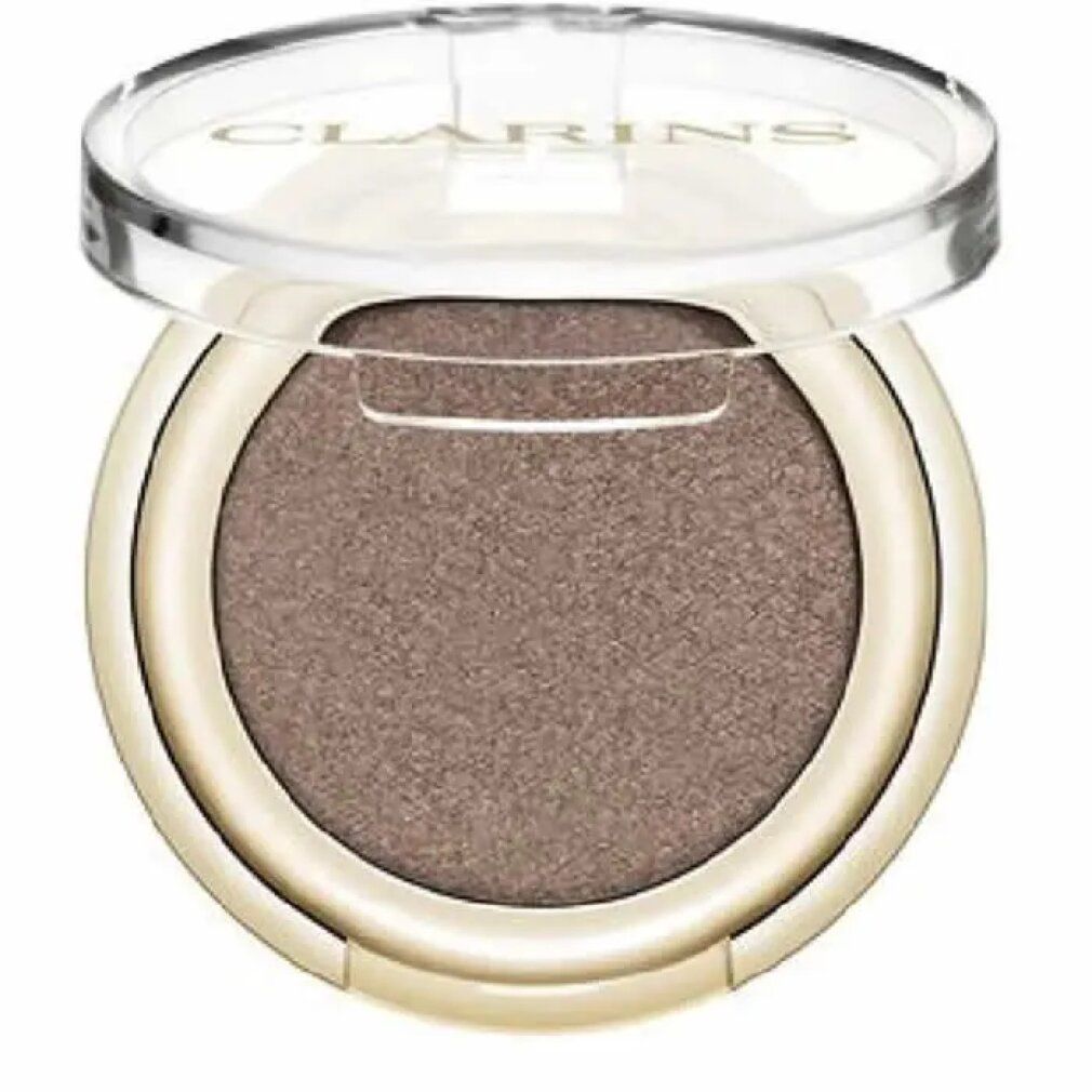Ombretto Clarins rotondo, dorato. Coperchio aperto. Interno: Satin Taupe. Scritta Clarins.