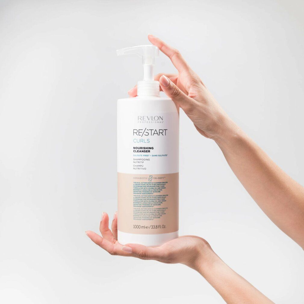 Flacone bianco con dosatore. Scritta Revlon Re-Start Curls. Testo in inglese e spagnolo. Mani che tengono il flacone.