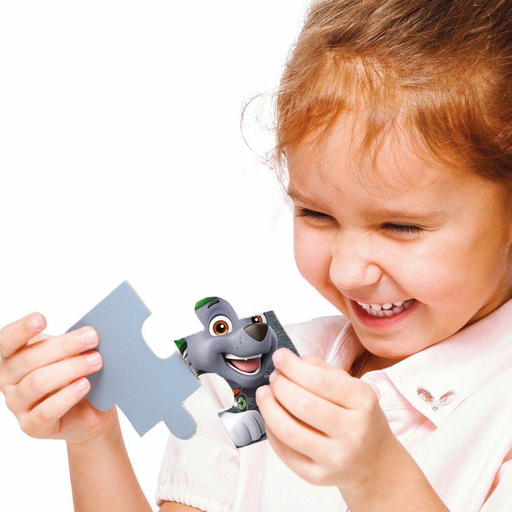 Bambino tiene un pezzo di puzzle con Rocky. Il bambino indossa una camicia rosa. Sfondo: bianco.