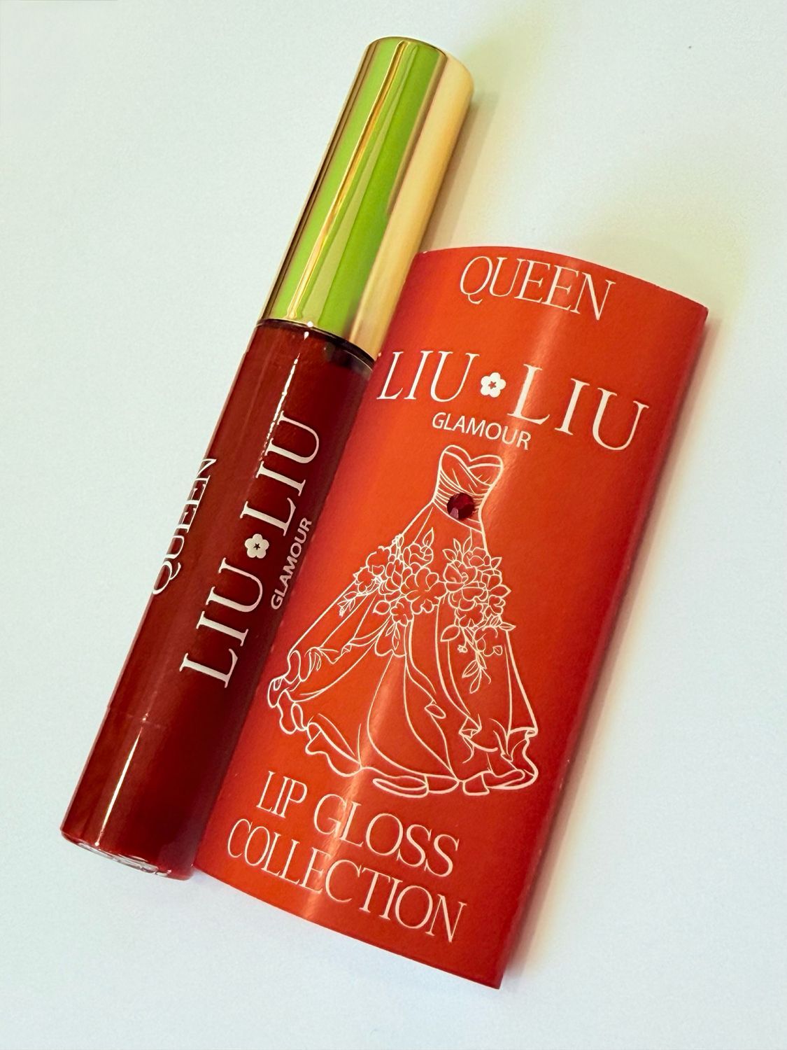 Lucidalabbra rosso e confezione rossa. Scritta: QUEEN LIU LIU Glamour. Confezione con illustrazione di abito da sera. Prodotto e confezione.