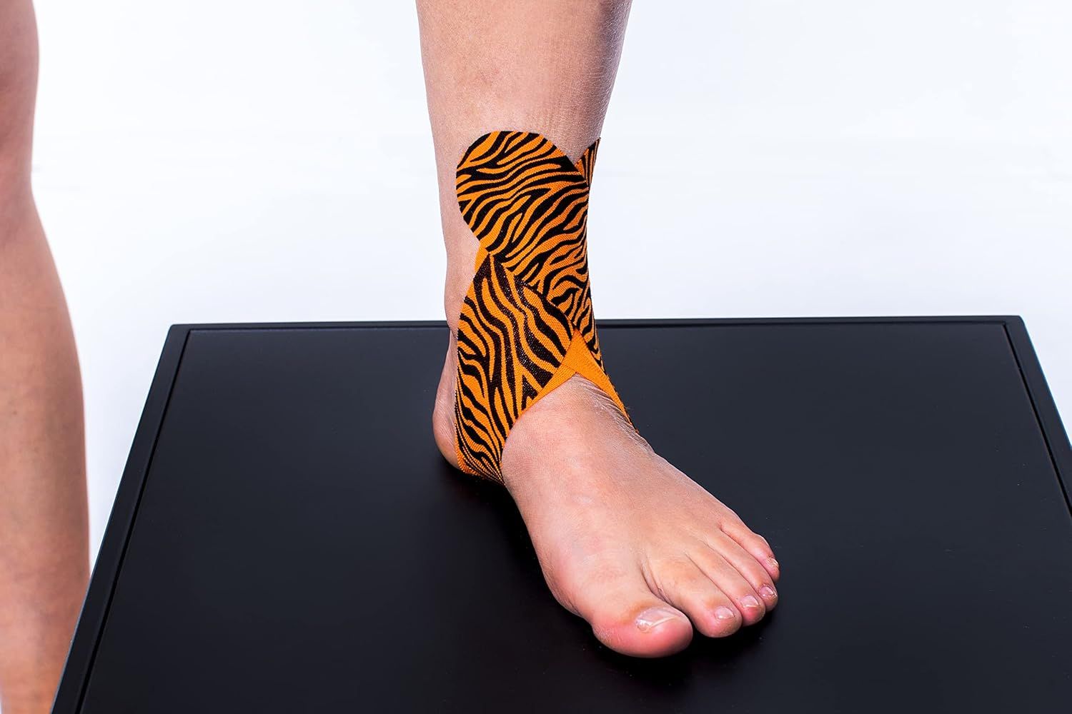 Piede e caviglia con CureTape Tiger. Arancione e nero. Su un piedistallo nero. Applicazione sulla caviglia.
