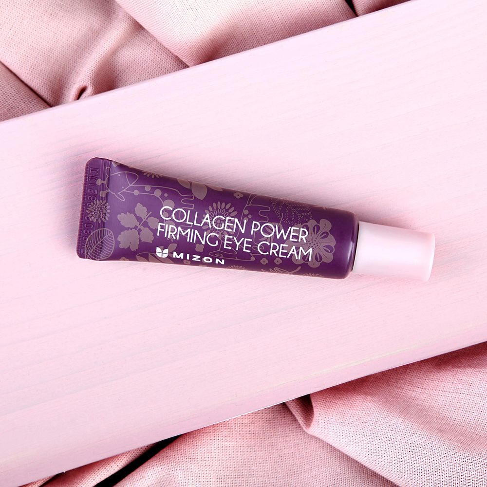 Tubo viola MIZON Collagen Power Firming Eye Cream su tessuto rosa. Tappo rosa. Testo: Collagen Power Firming Eye Cream.