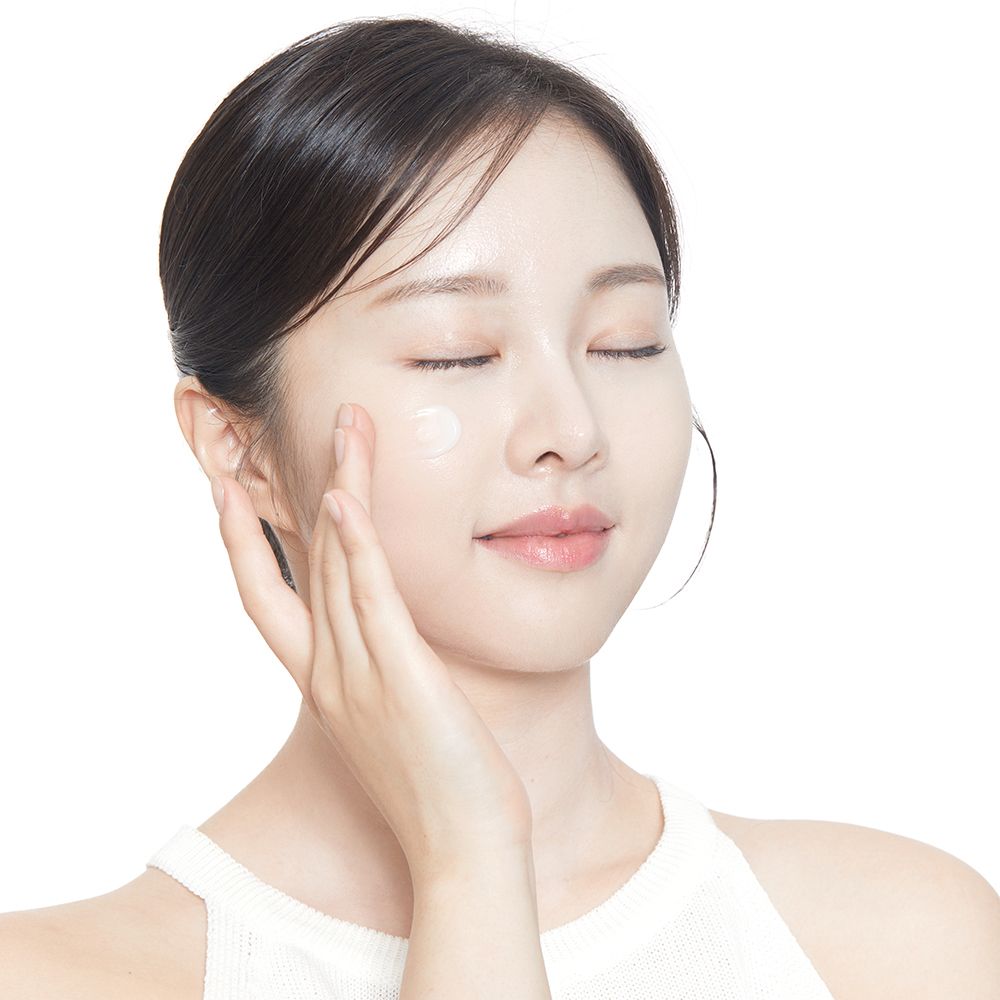 Viso di una donna che applica la crema sulla pelle. Occhi chiusi, crema sulla guancia.