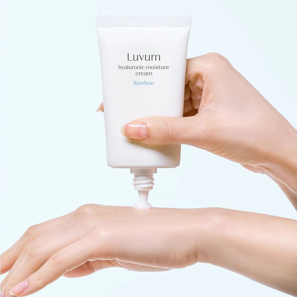 Mano che preme la crema da un tubo bianco. Scritta: LUVUM, crema idratante all'acido ialuronico, bambù. Crema applicata sulla mano.