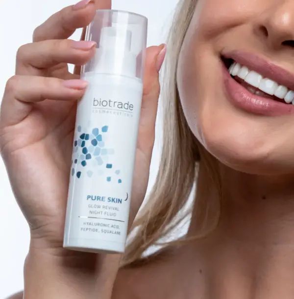 Flacone bianco con pompa e tappo trasparente. Scritta: Pure Skin Glow Revival Night Fluid. Prodotto tenuto da una persona.