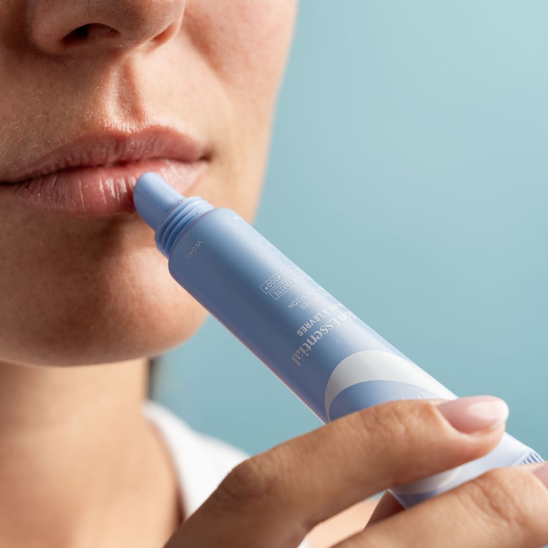 Persona applica balsamo labbra in tubo azzurro chiaro. Primo piano delle labbra. Nome del prodotto visibile.