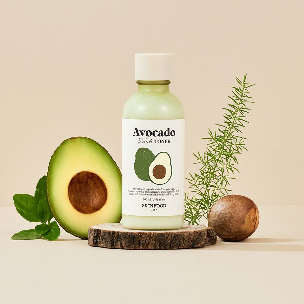 Flacone di toner verde con illustrazione di avocado. Su ceppo di legno, metà avocado, ramo e nocciolo.