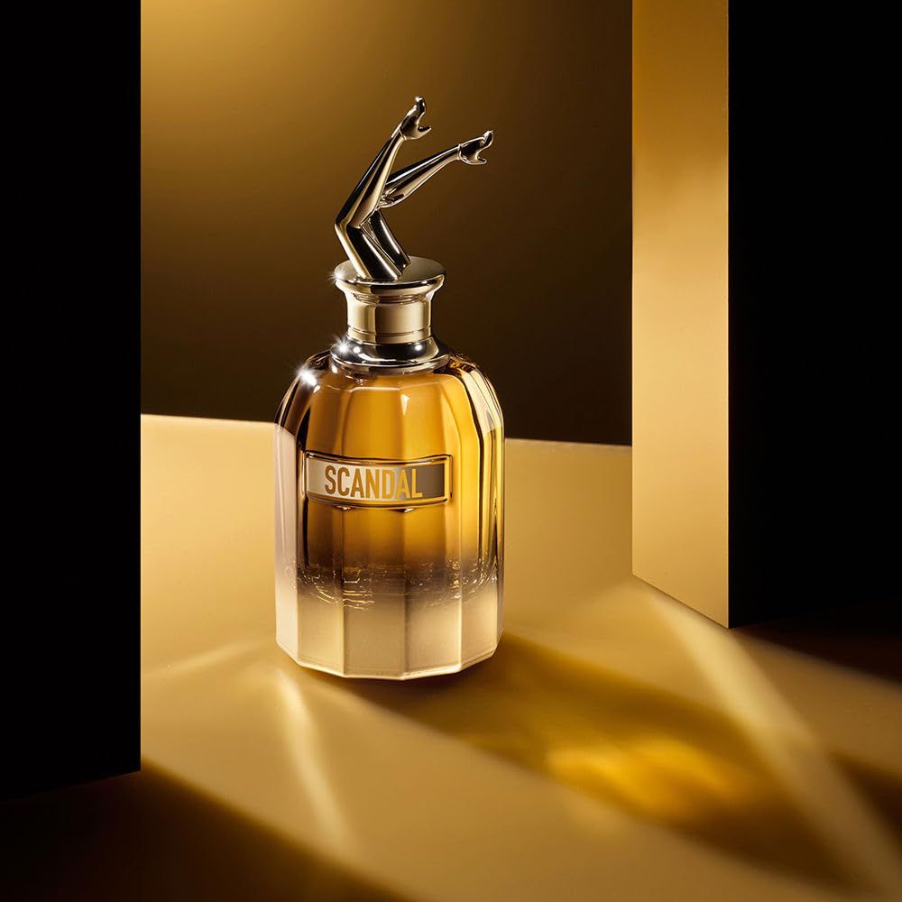Flacone di profumo con gambe dorate come tappo. Flacone dorato con scritta "SCANDAL".