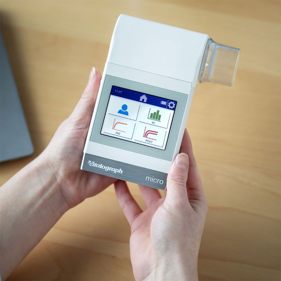 Persona che tiene uno spirometro portatile Vitalograph micro con display touchscreen che mostra grafici della funzione polmonare.