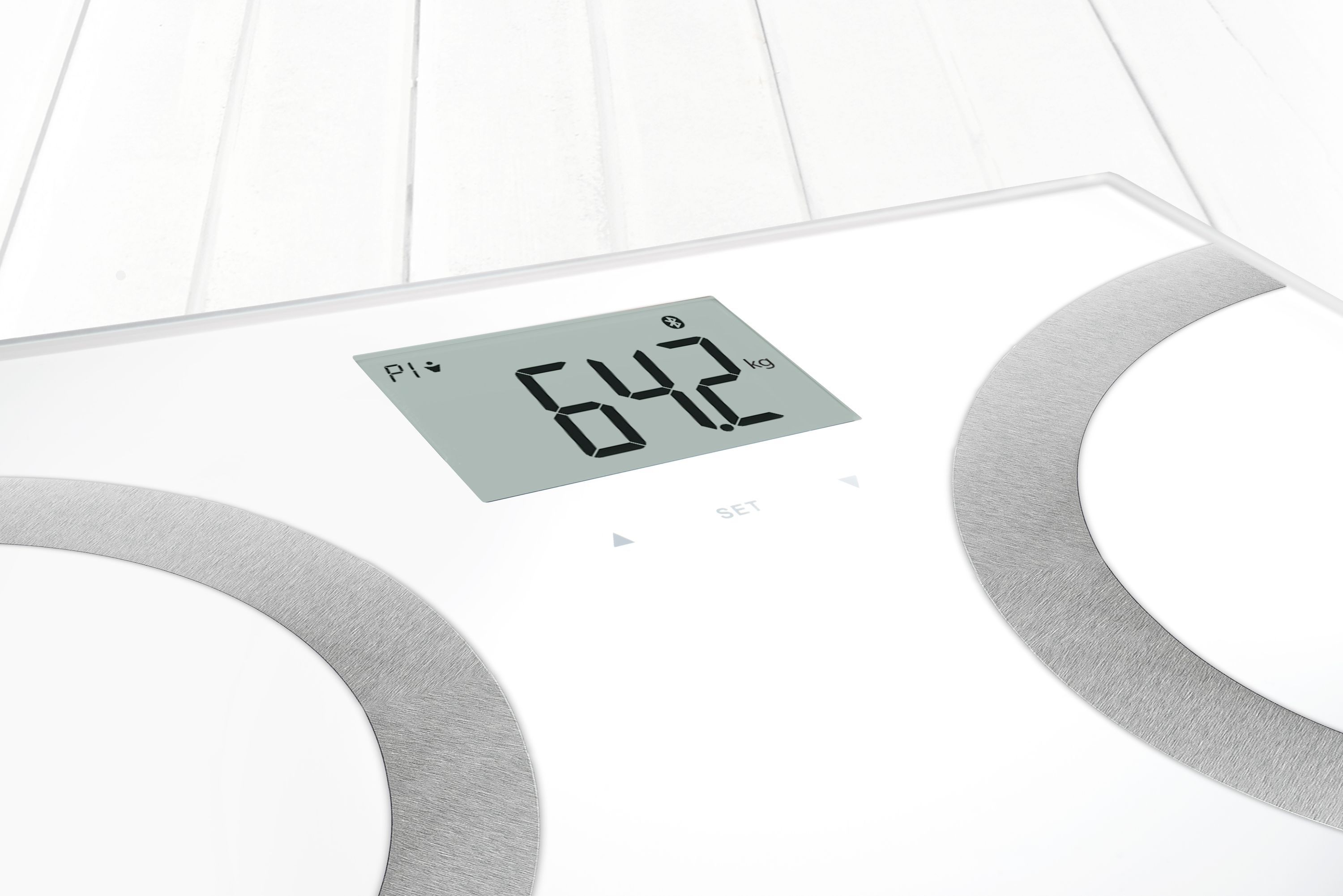 Primo piano di una bilancia per analisi corporea bianca. Mostra 64,2 kg sul display digitale. Elementi grigi a forma di semicerchio.