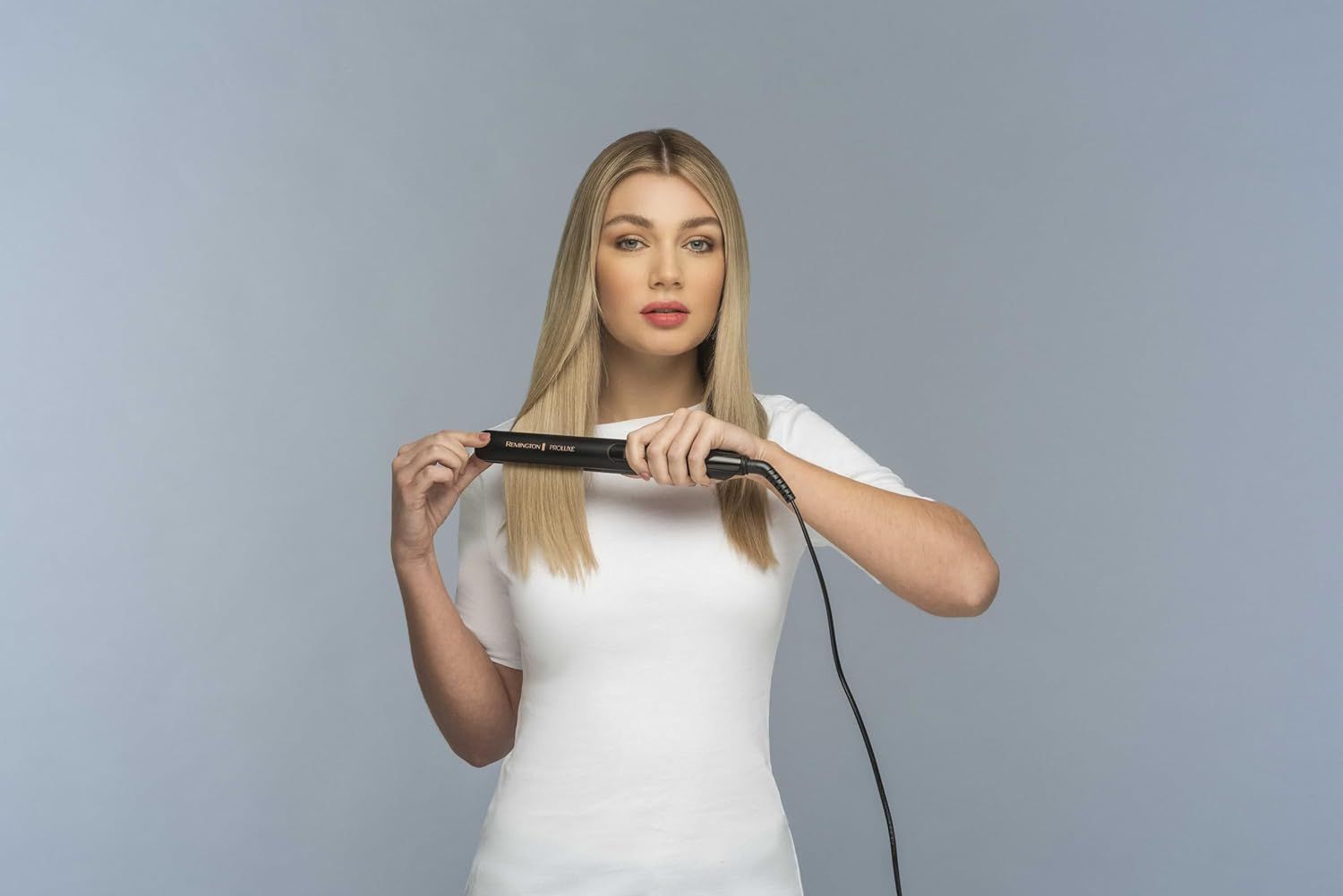 Donna bionda tiene una piastra nera. Guarda la fotocamera. La piastra è in uso.