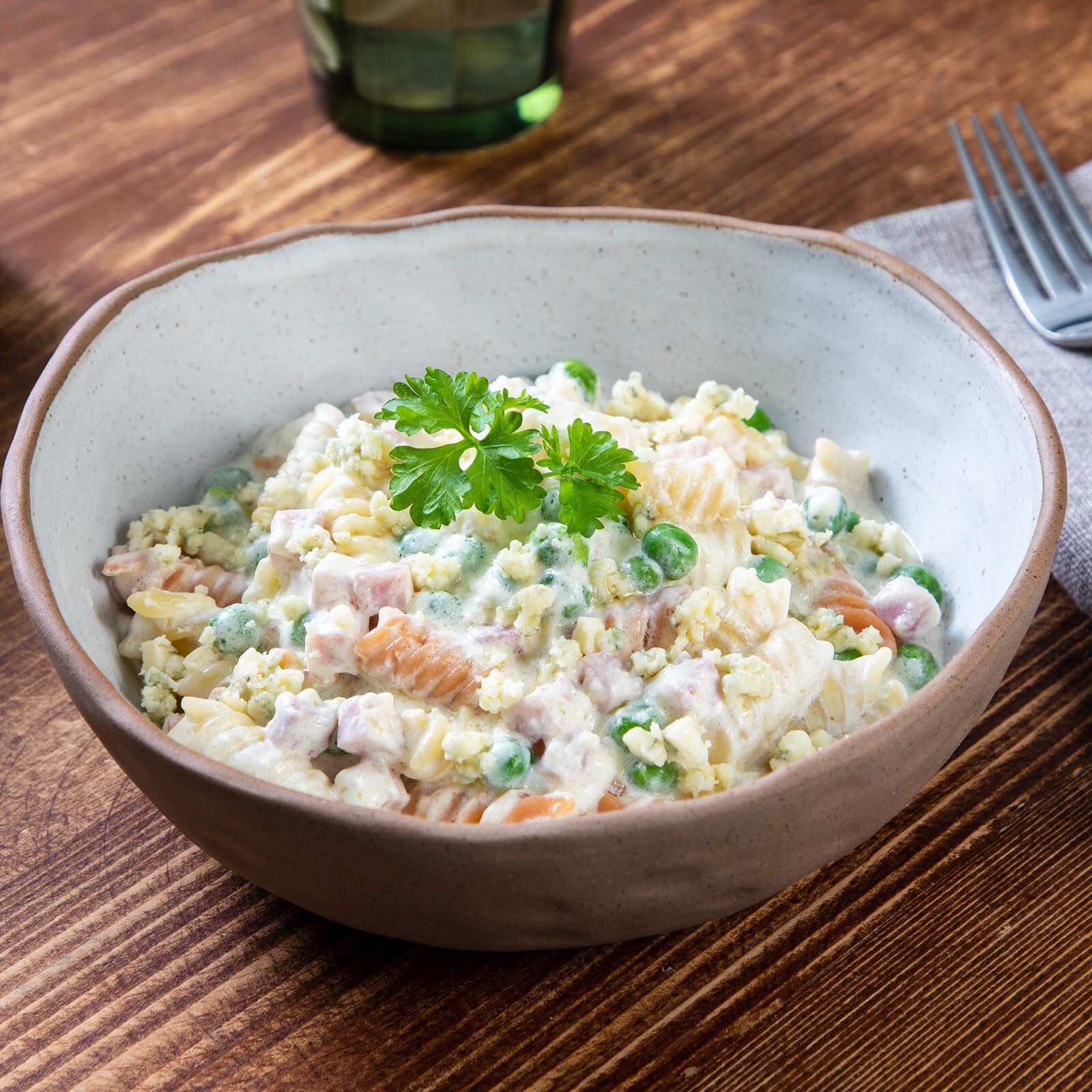 Ciotola di fusilli tricolore con piselli, prosciutto e salsa. Su tavolo di legno.