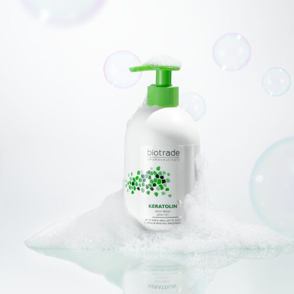 Dispenser bianco con erogatore verde, circondato da schiuma e bolle di sapone. Scritta Biotrade e Keratolin.