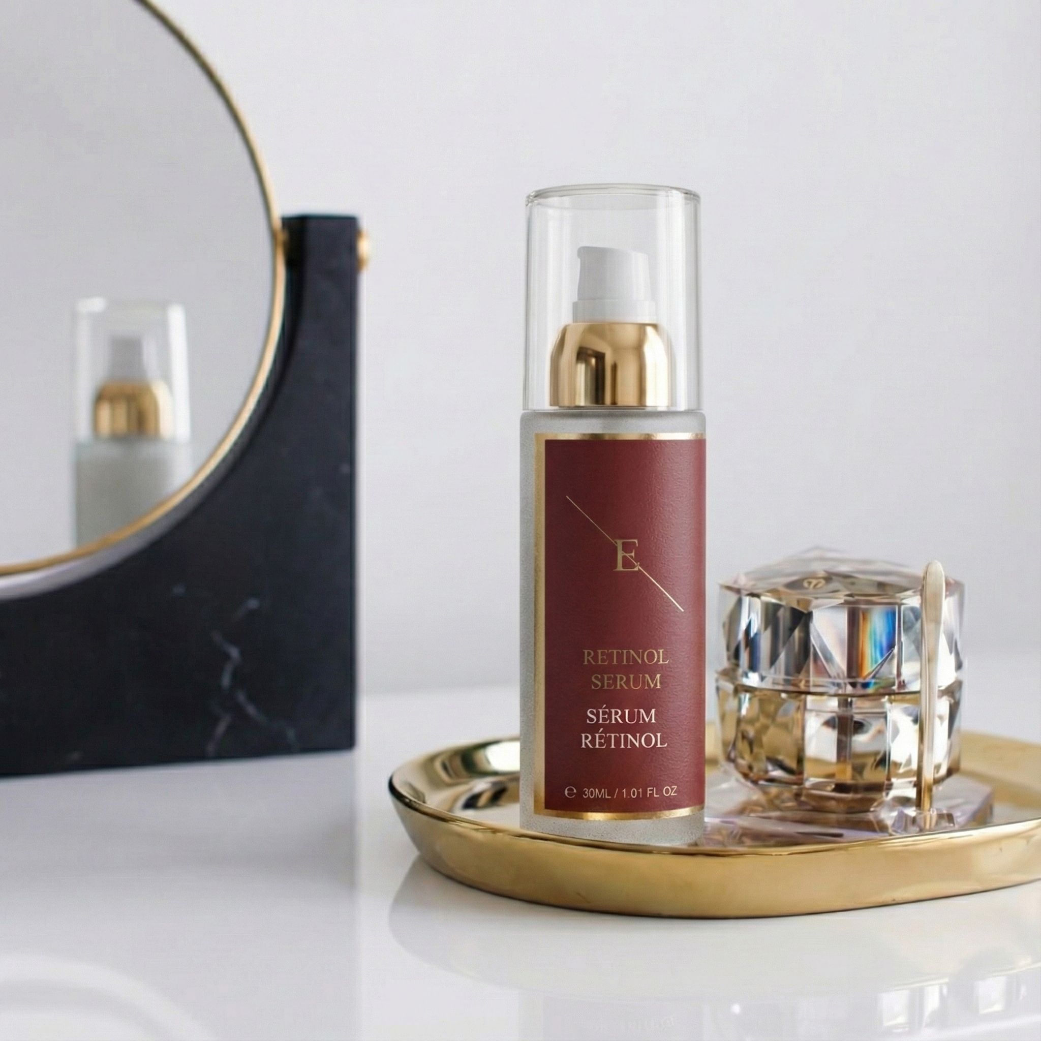 Flacone di siero su vassoio dorato, accanto a un portagioie e uno specchio. Etichetta rossa con testo: Retinol Serum, Sérum Rétinol.