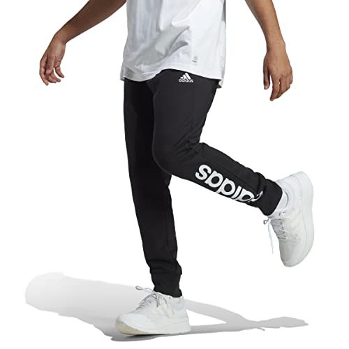 Uomo con pantaloni Adidas neri con grande logo laterale e scarpe bianche.