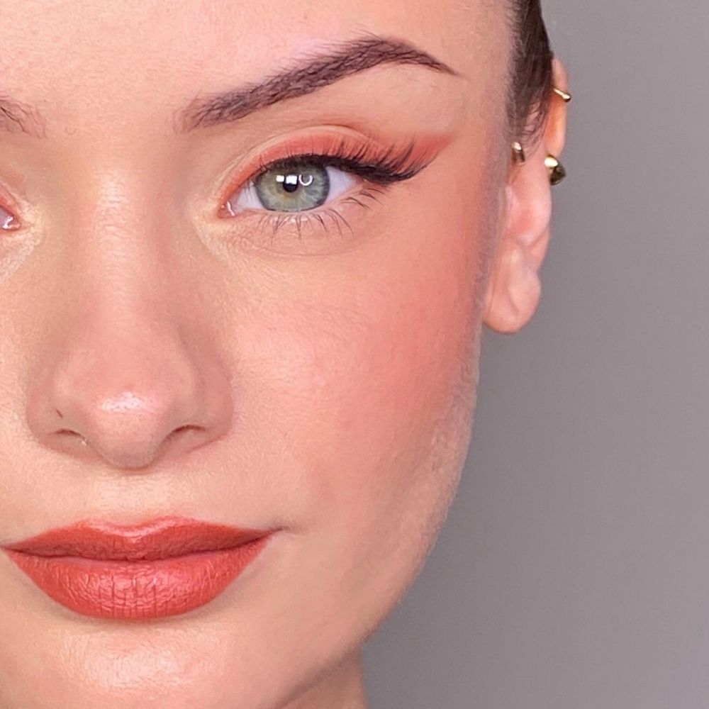 Primo piano di un viso con occhi, guance e labbra truccate. Rossetto color corallo. Tono della pelle chiaro.