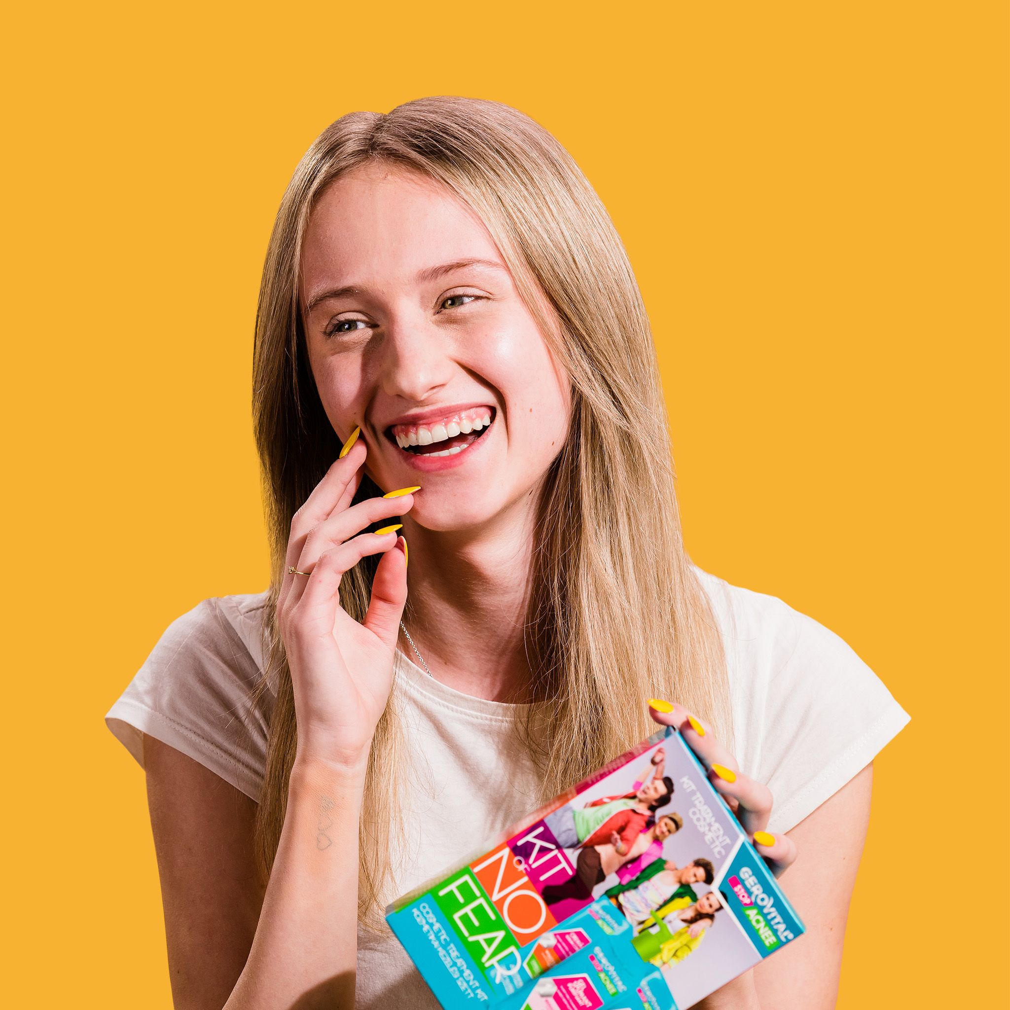 Una donna tiene in mano una confezione del kit Gerovital Stop Acnee. Sfondo giallo. La confezione mostra immagini di prodotti e persone.
